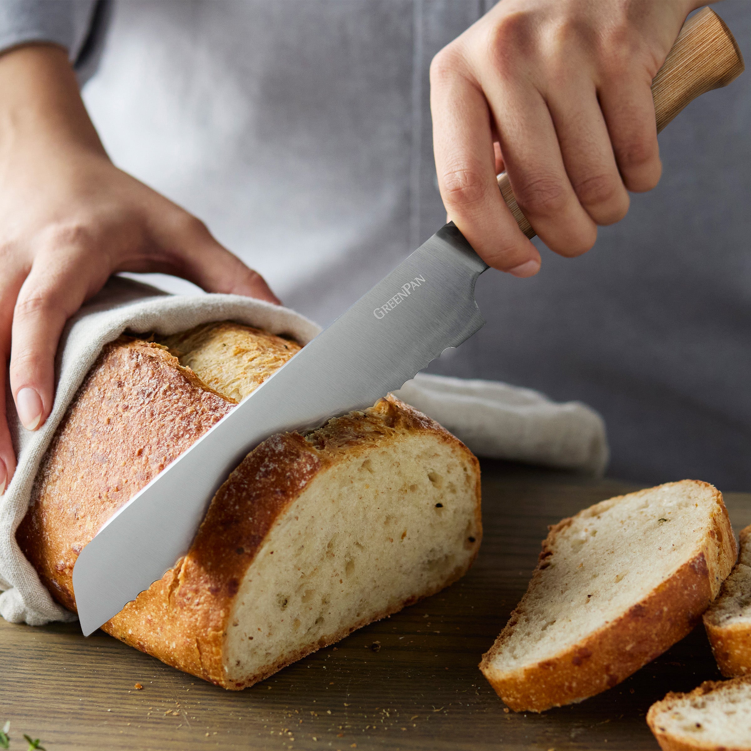 Person slicing bread with a knife on a wooden cutting board