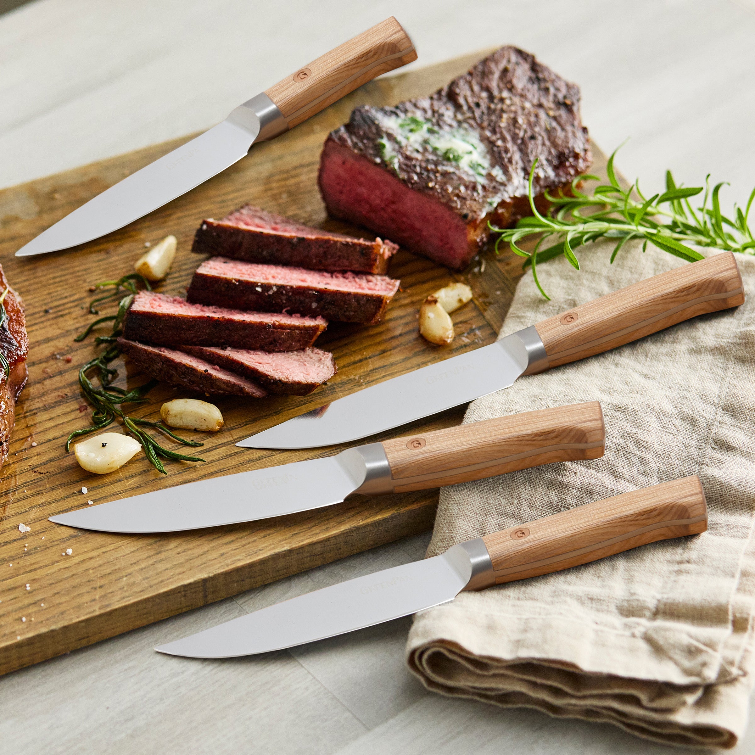 Wooden cutting board with sliced steak and four steak knives on a countertop