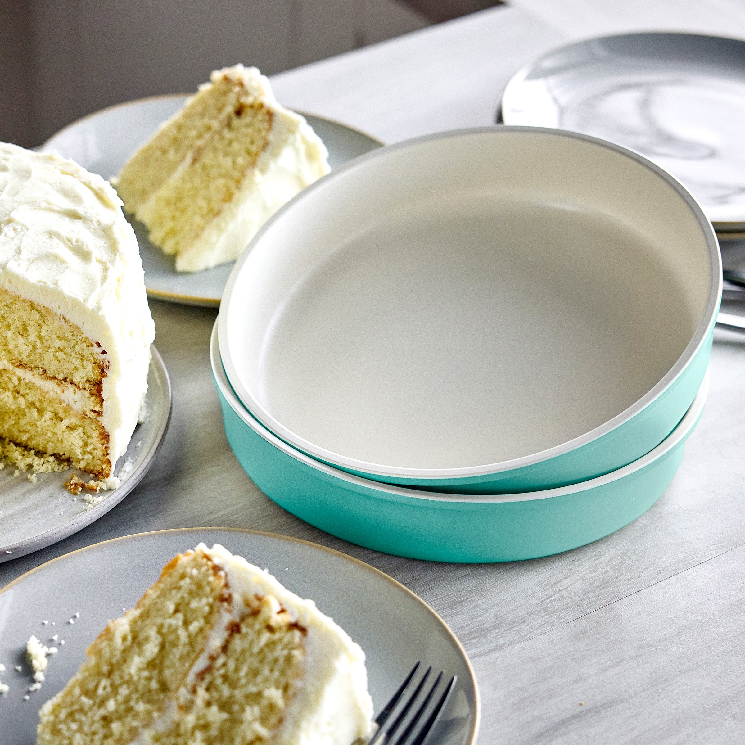 Two turquoise round cake pans on a table with slices of cake and plates.