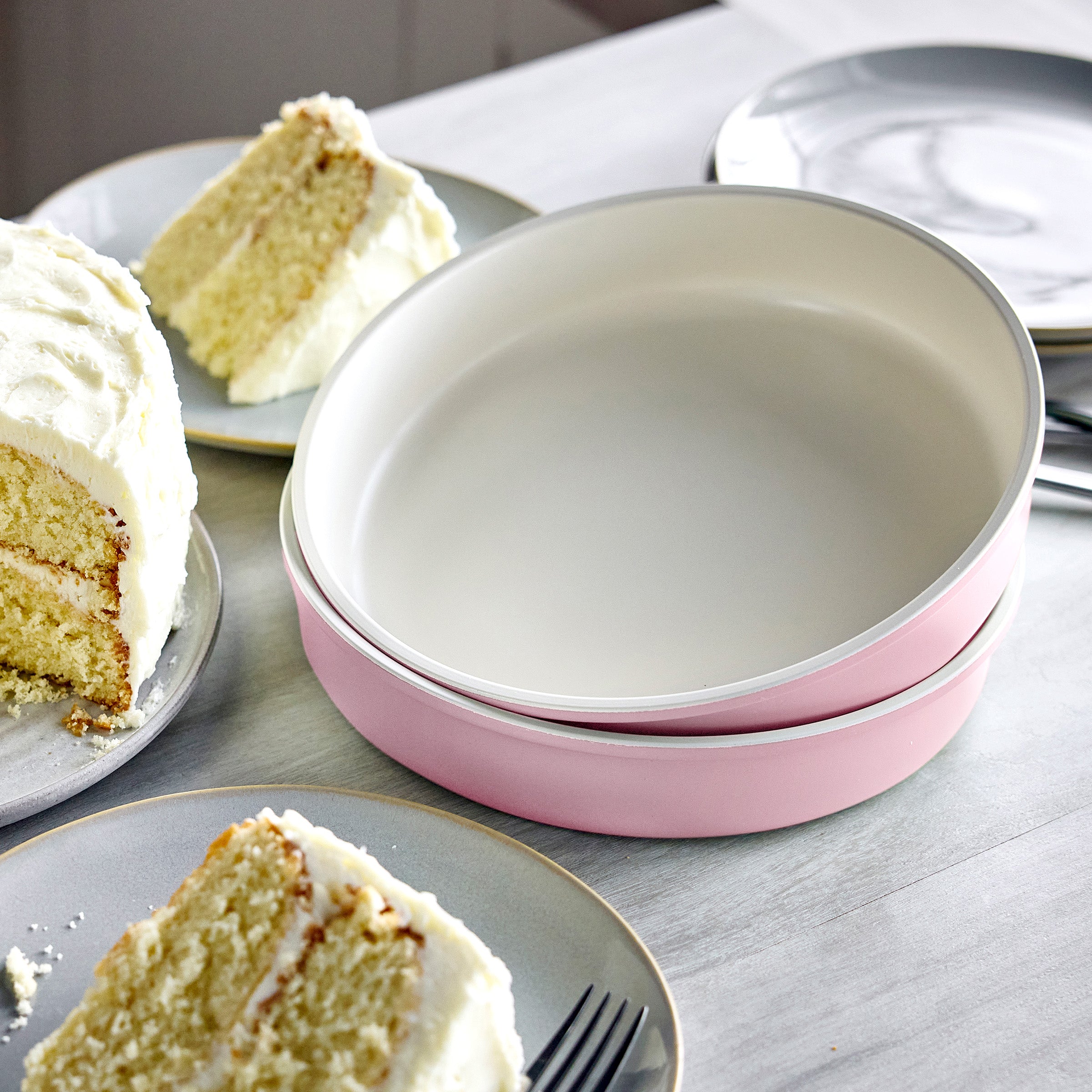 Two pink round cake pans on a table with slices of cake and plates.