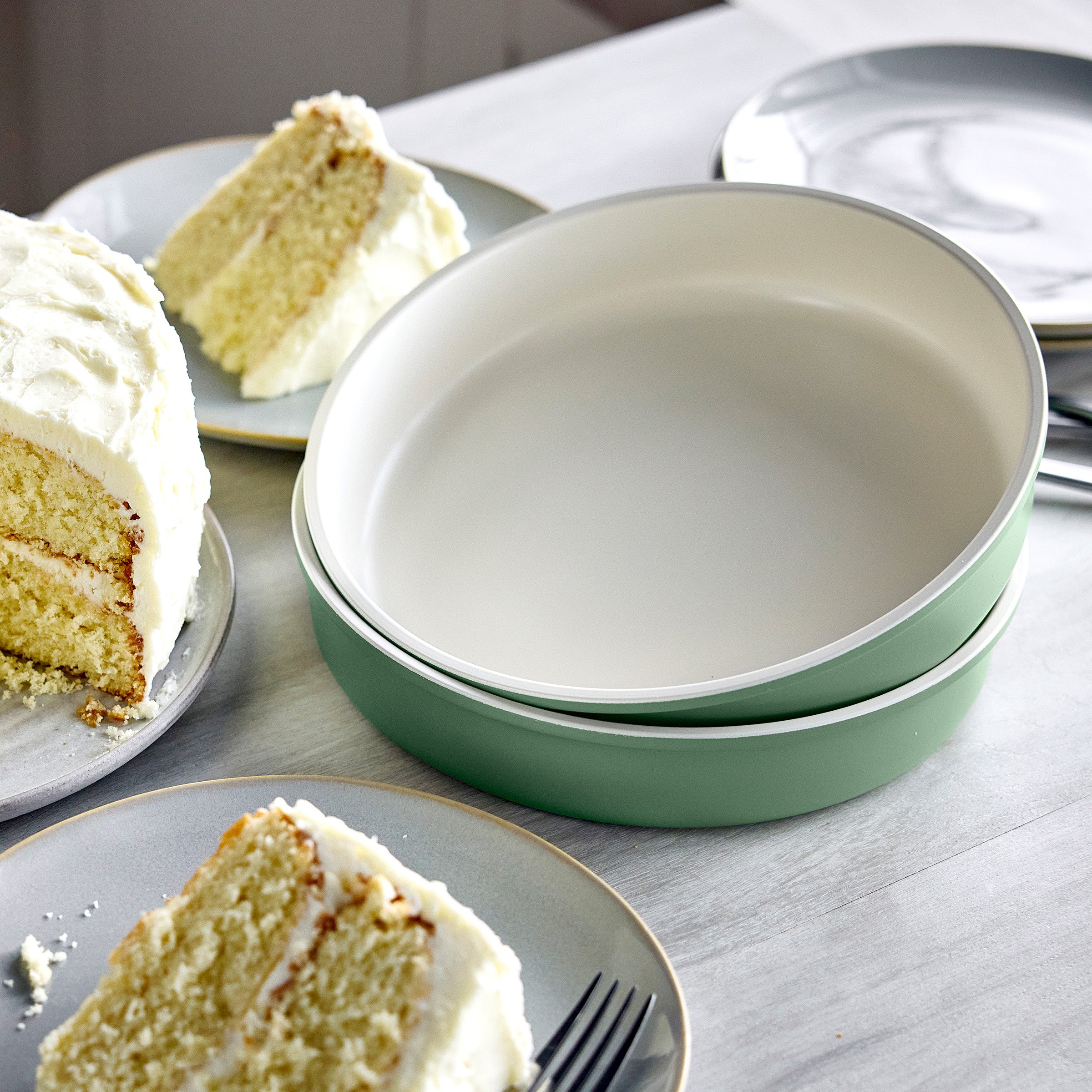 Two green round cake pans on a table with slices of cake and plates.
