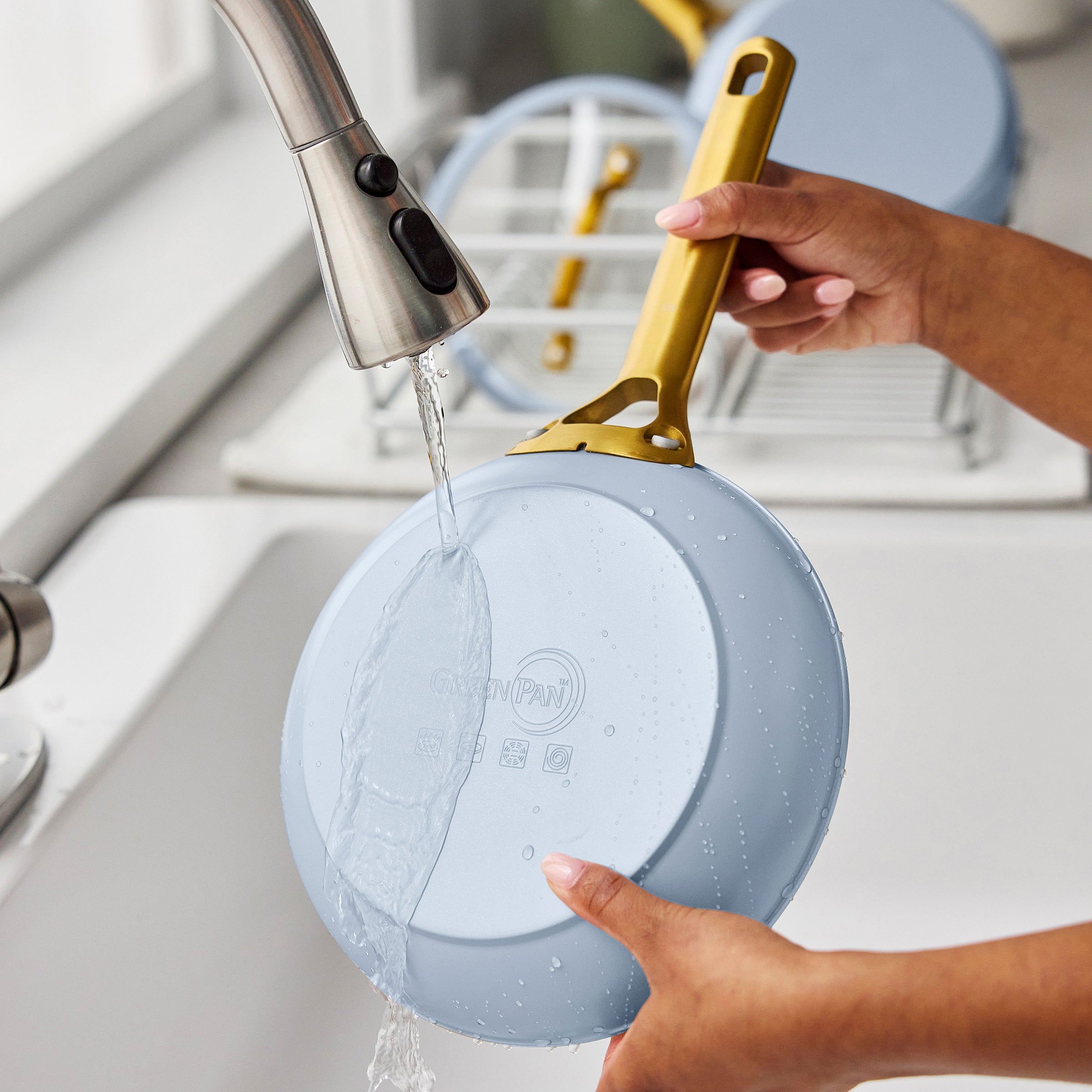 Person washing a light blue frying pan with a gold handle in a kitchen sink
