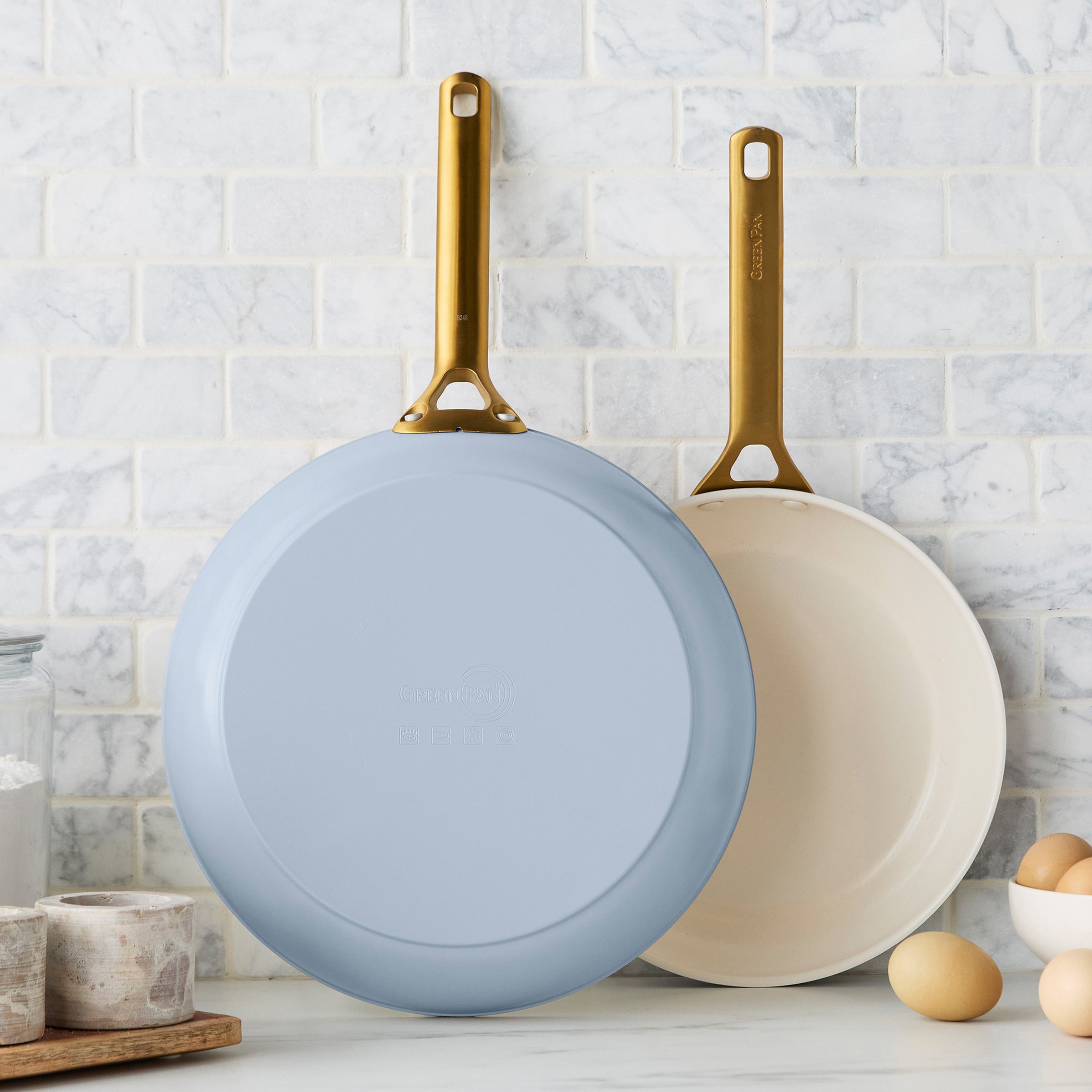 Two light blue frying pans with gold handles on a kitchen counter.