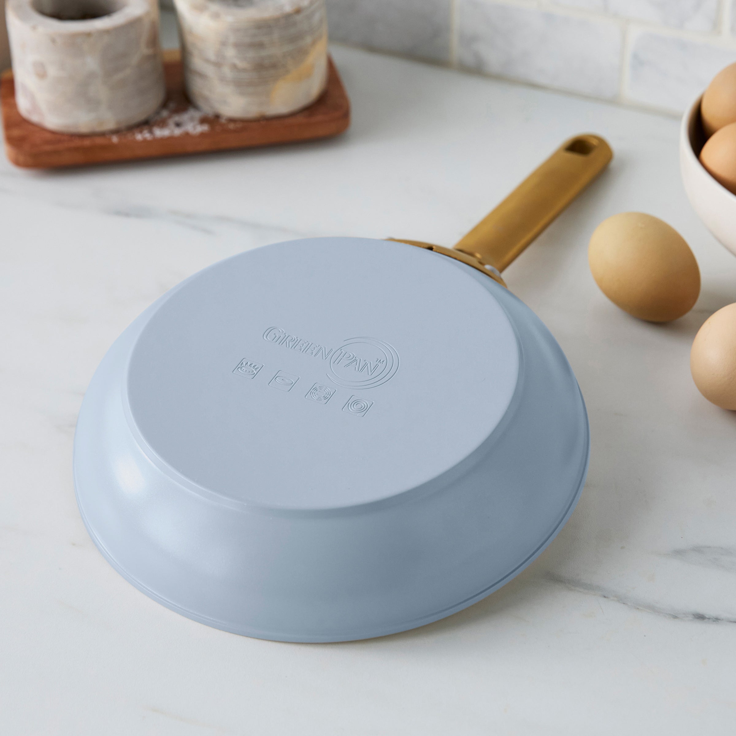 Light blue frying pan with a gold handle on a kitchen counter.