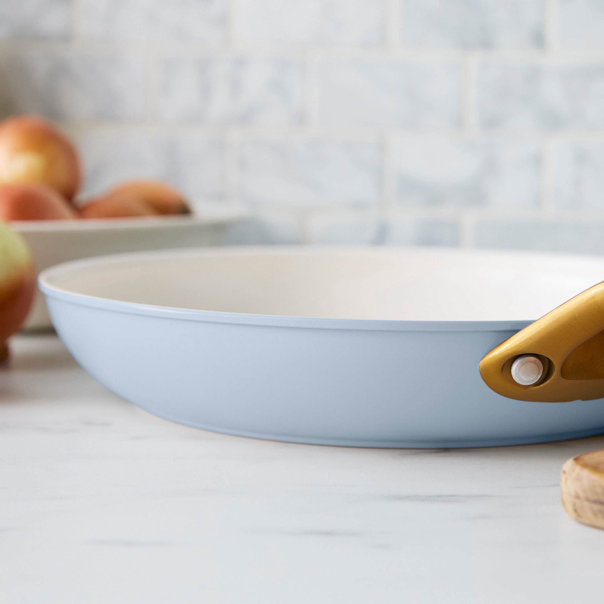 Light blue frying pan with a gold handle on a kitchen counter