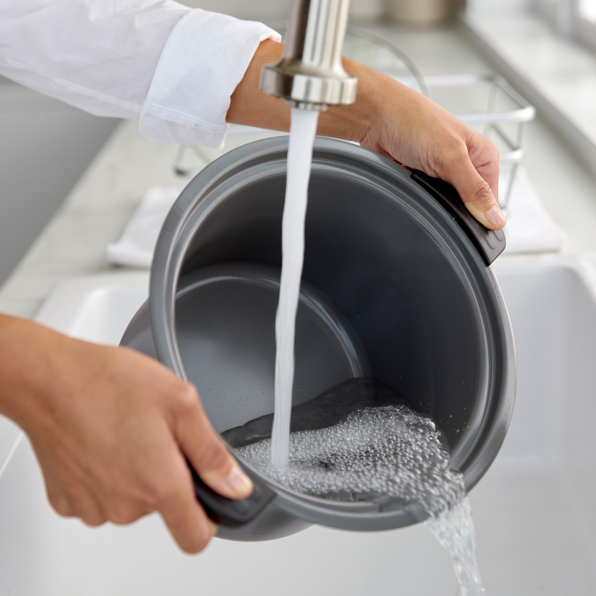 Person washing a pot under running water in a kitchen sink.