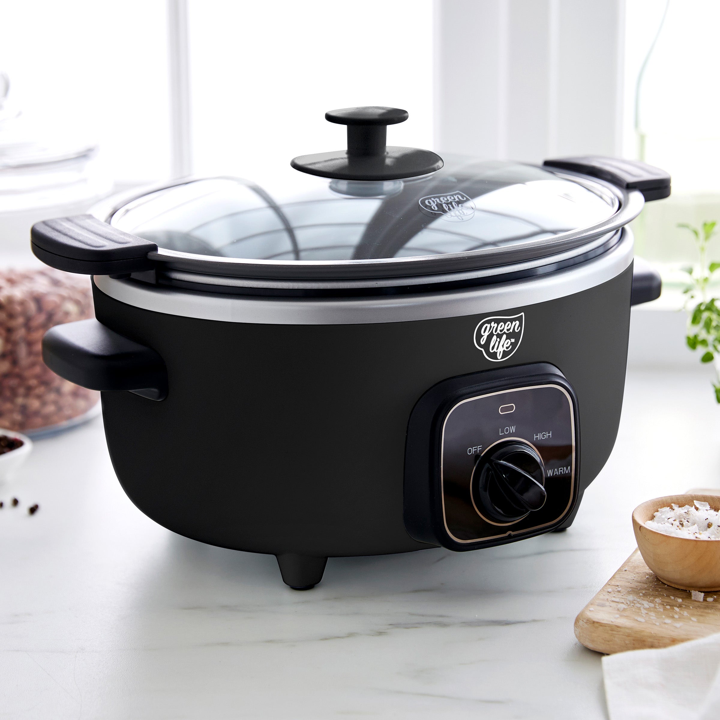 Black electric slow cooker with a glass lid on a kitchen counter.