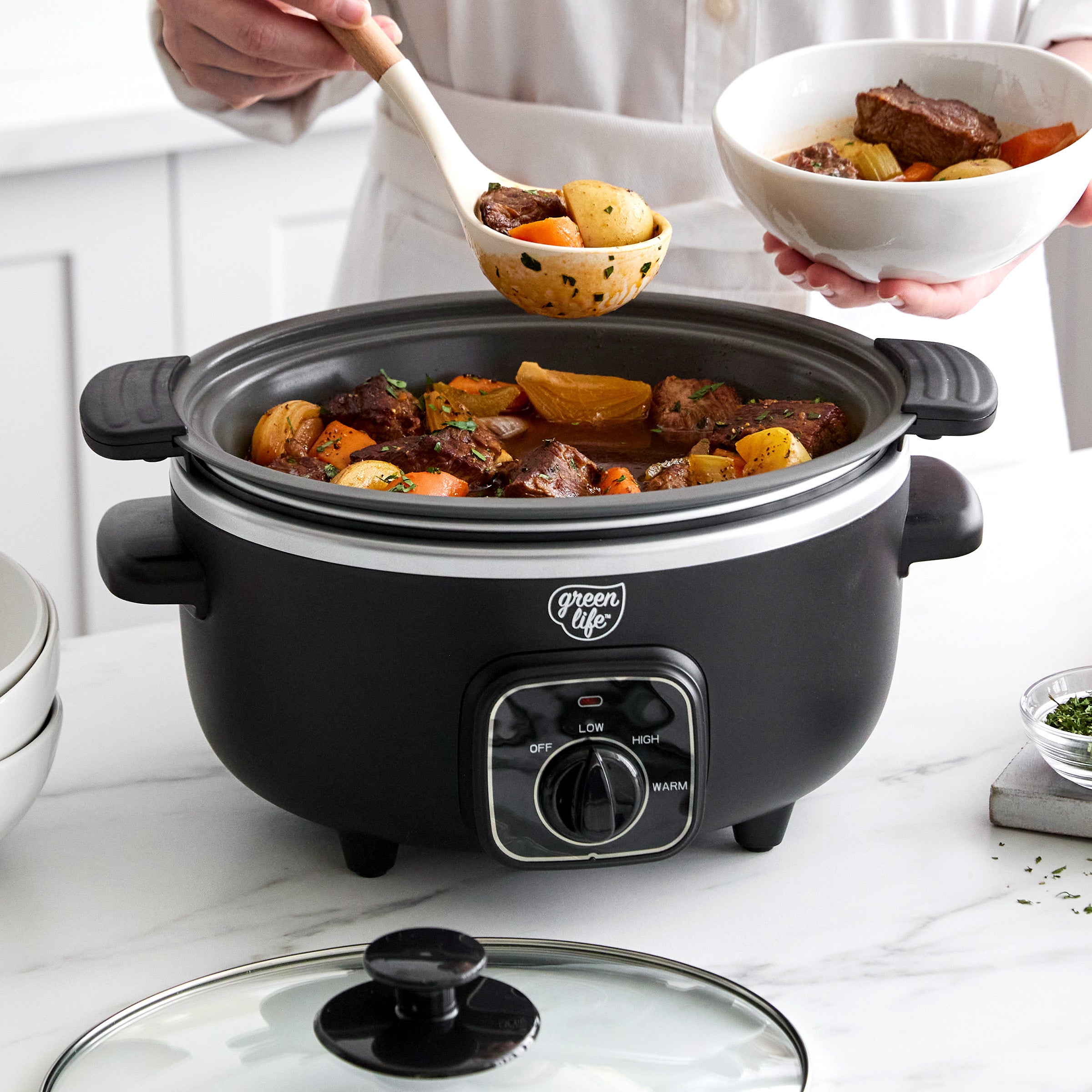 Black slow cooker with food being served from it on a kitchen counter.