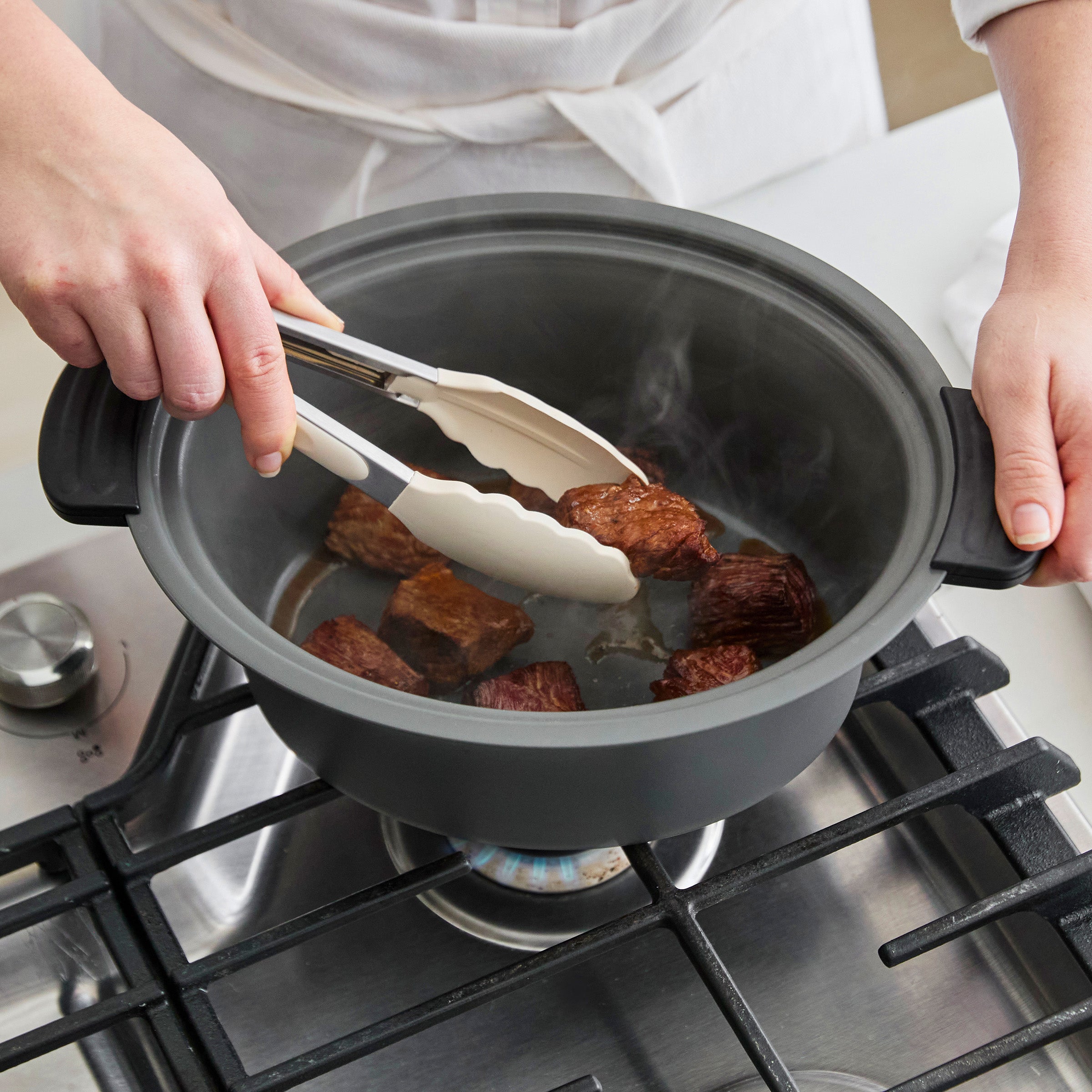 Person using tongs to handle food in a pot on a stove