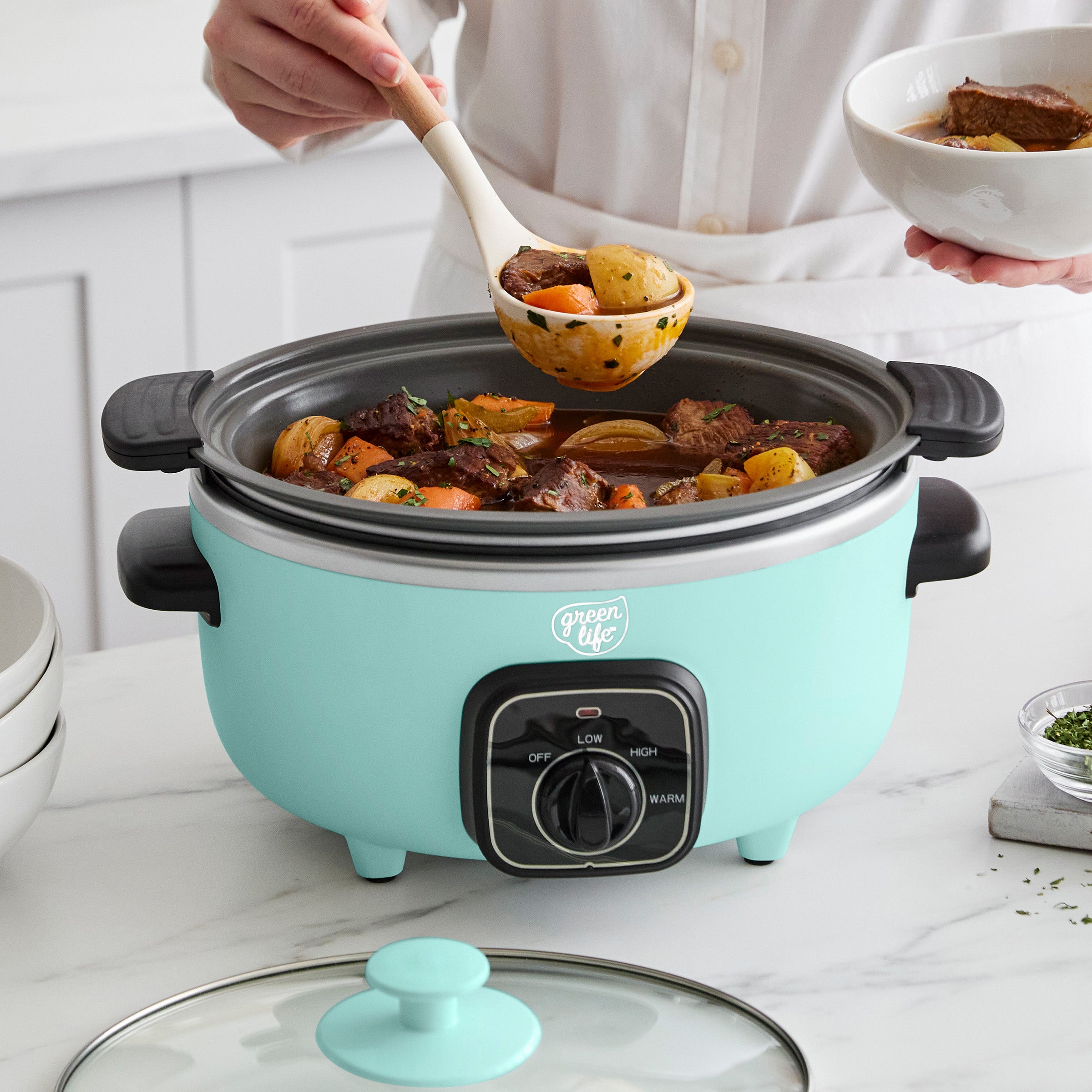 Turquoise slow cooker with food being served from it on a kitchen counter.
