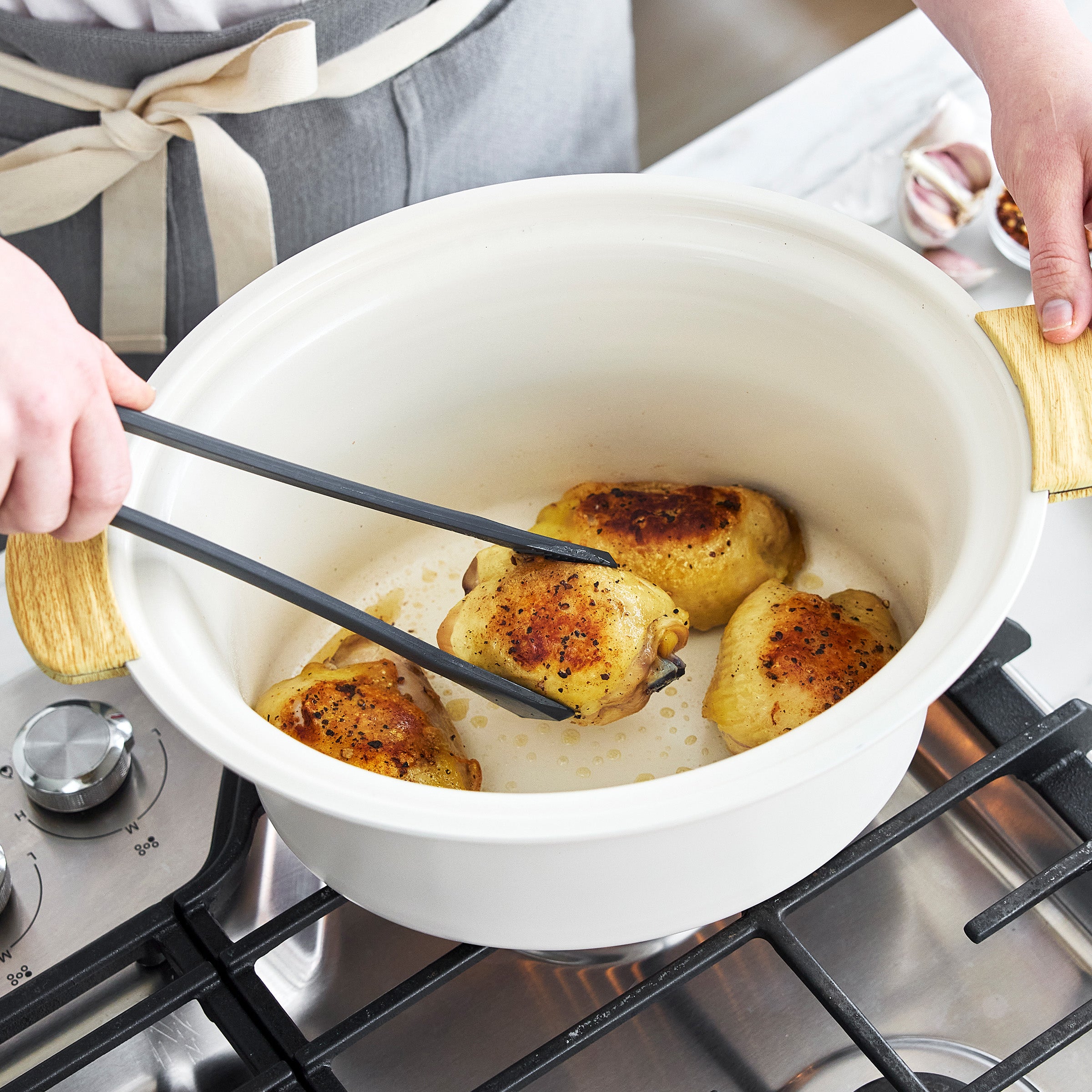 Person cooking chicken in a pot on a stove using tongs.