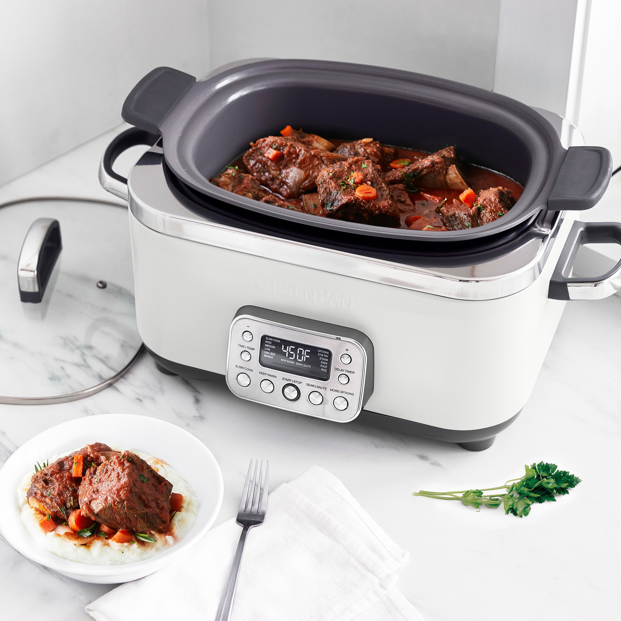 Cream slow cooker with digital display on a marble countertop, containing stewed meat and vegetables.