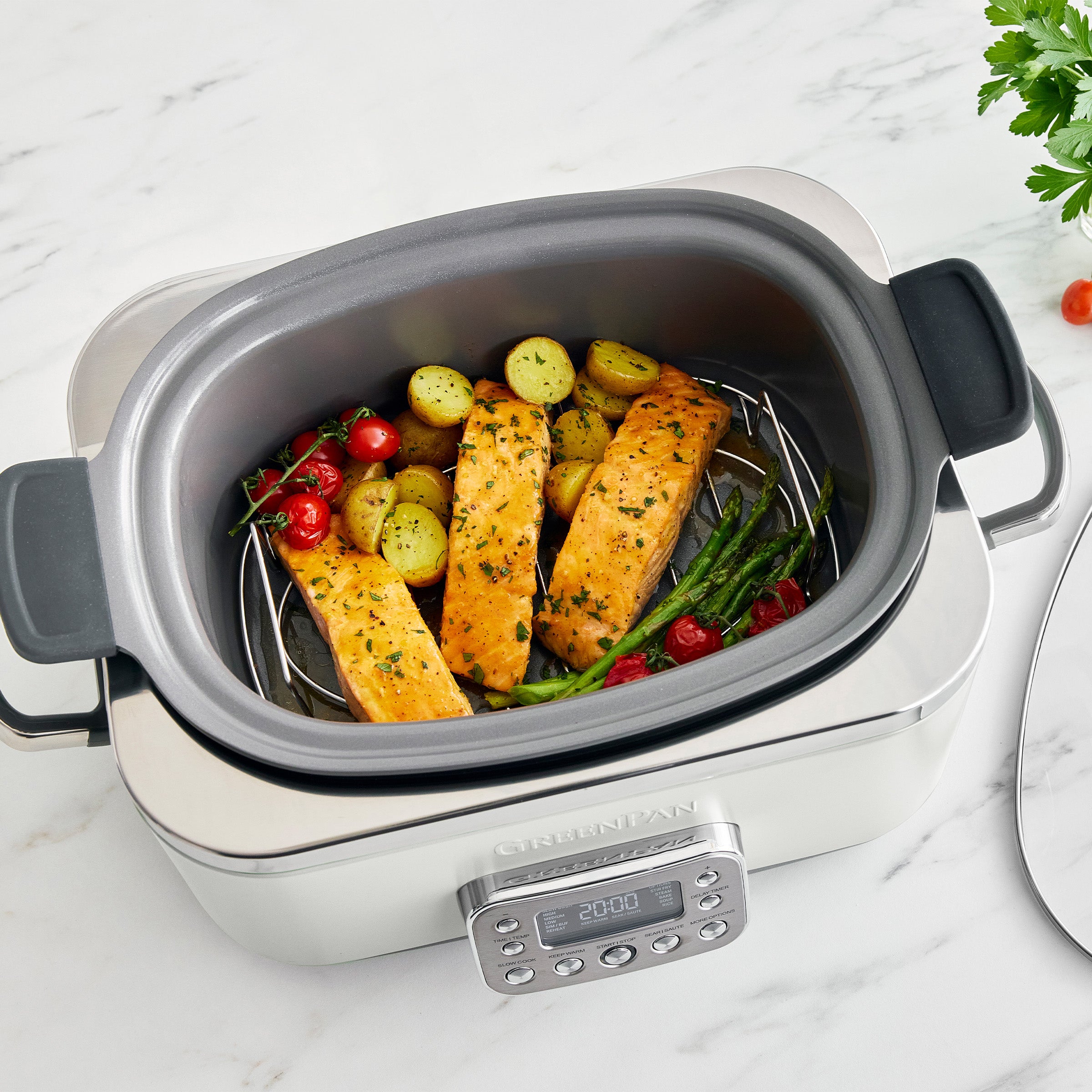 Cream slow cooker with salmon and vegetables on a marble surface