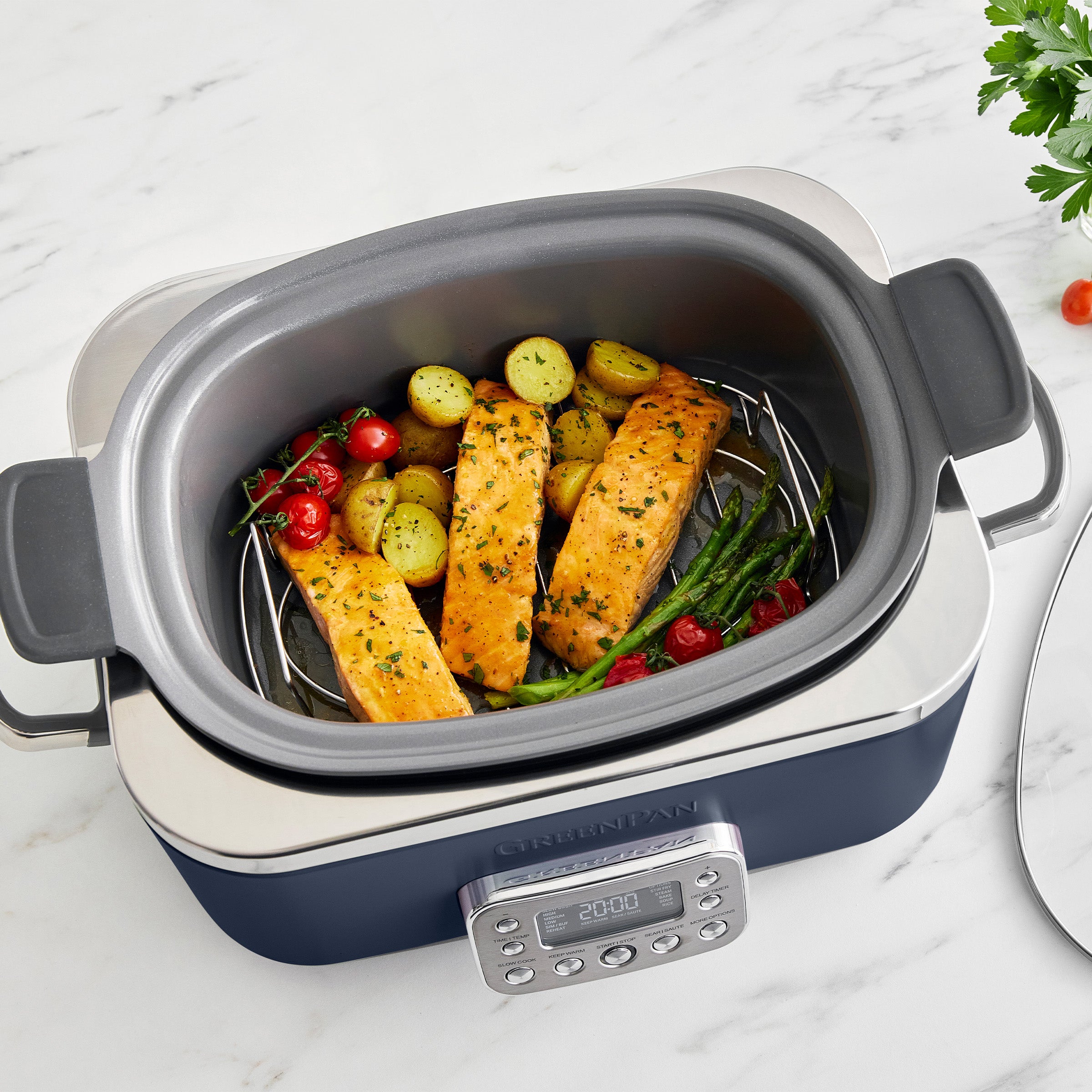 Blue slow cooker with salmon and vegetables on a marble surface