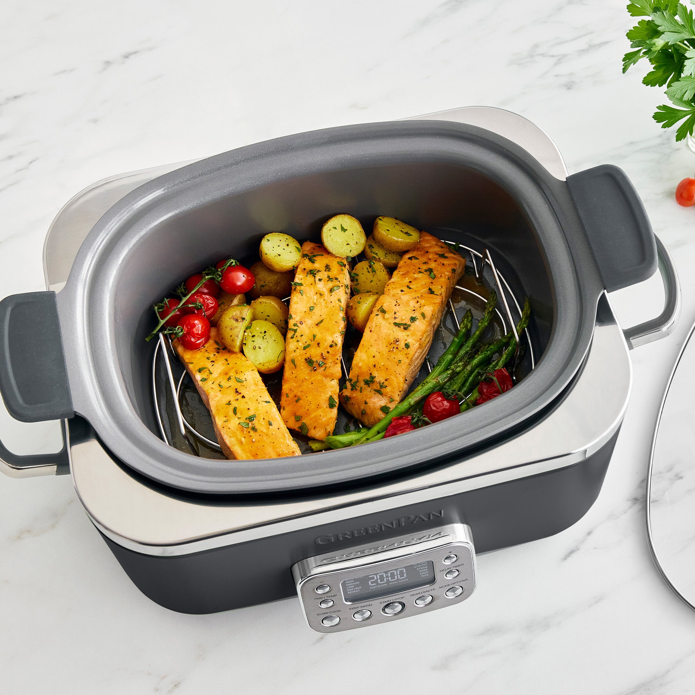 Gray slow cooker with salmon and vegetables on a marble surface