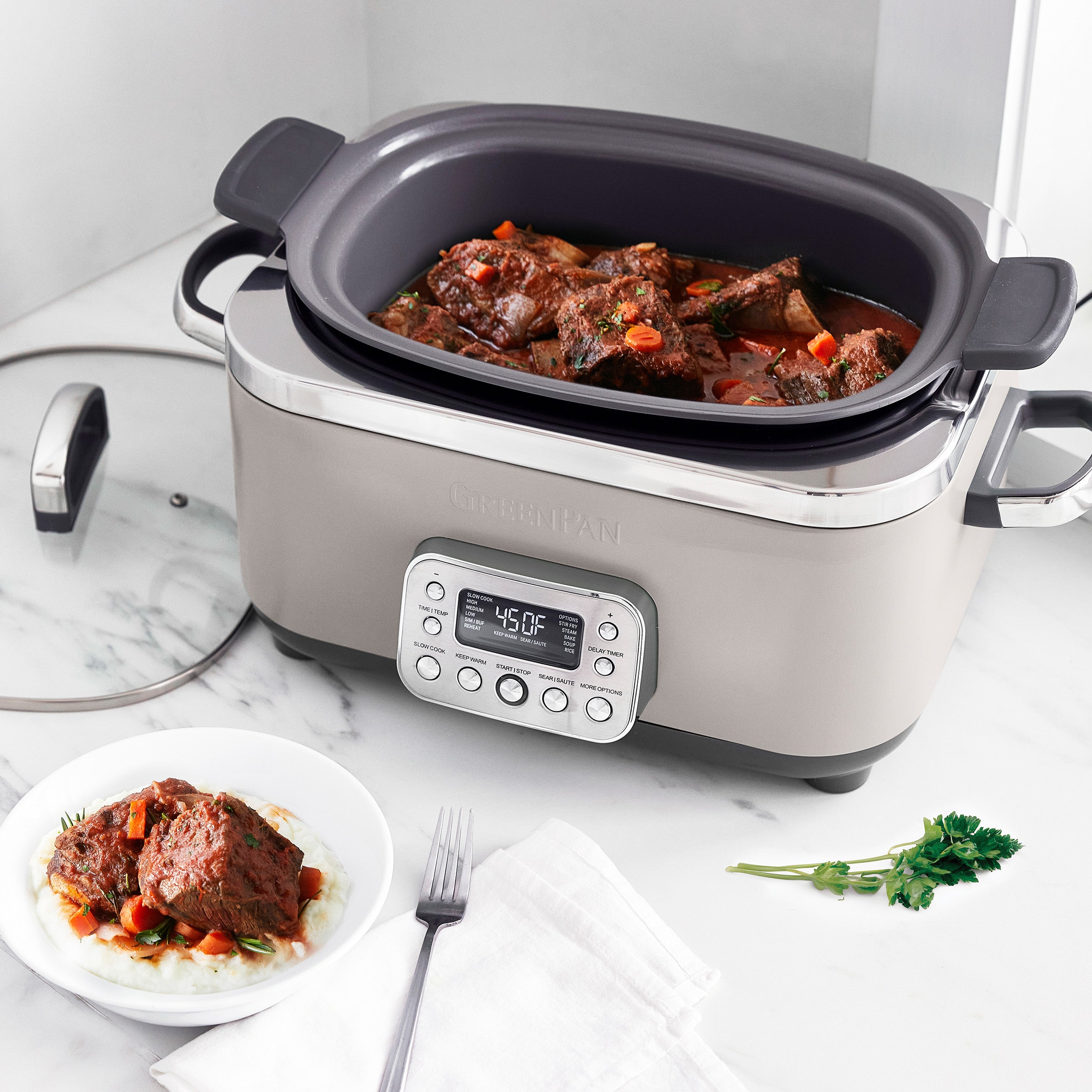 Taupe slow cooker with digital display on a marble countertop, containing stewed meat and vegetables.