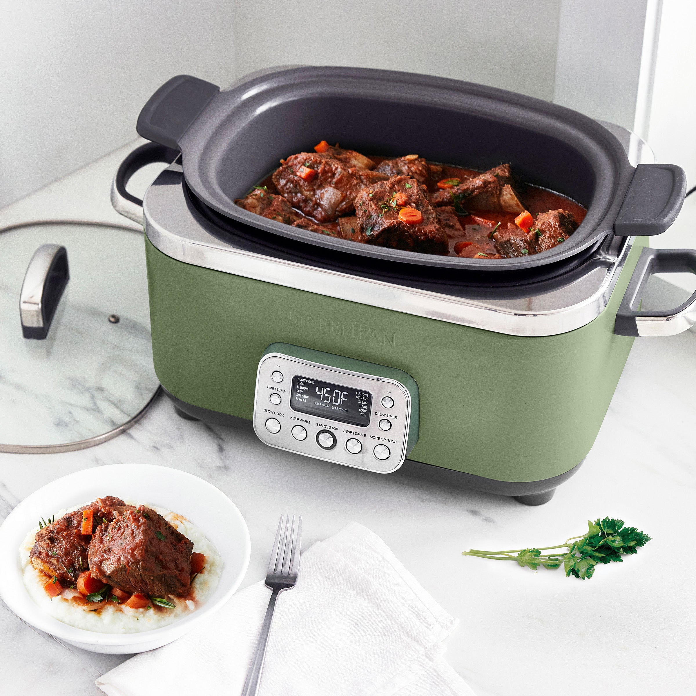 Green slow cooker with digital display on a marble countertop, containing stewed meat and vegetables.