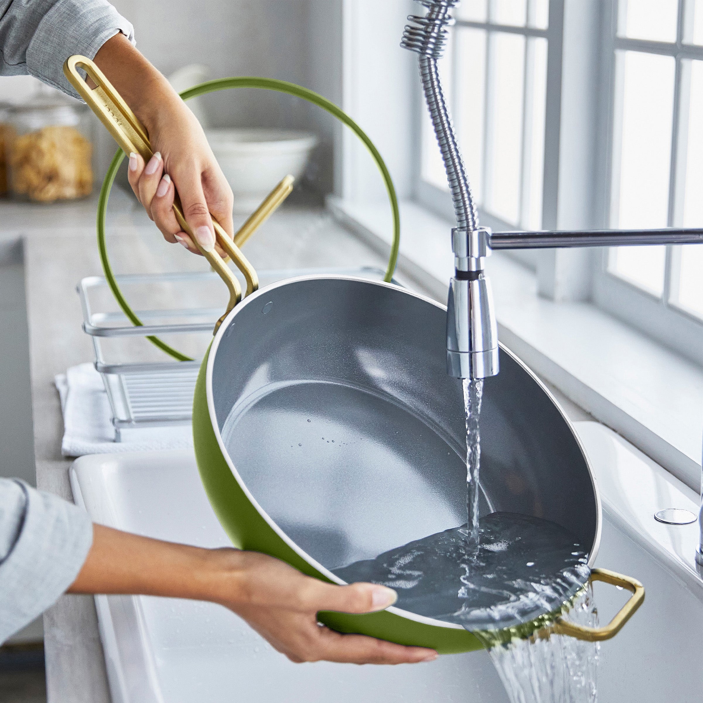 Person washing a pan under running water in a kitchen sink.