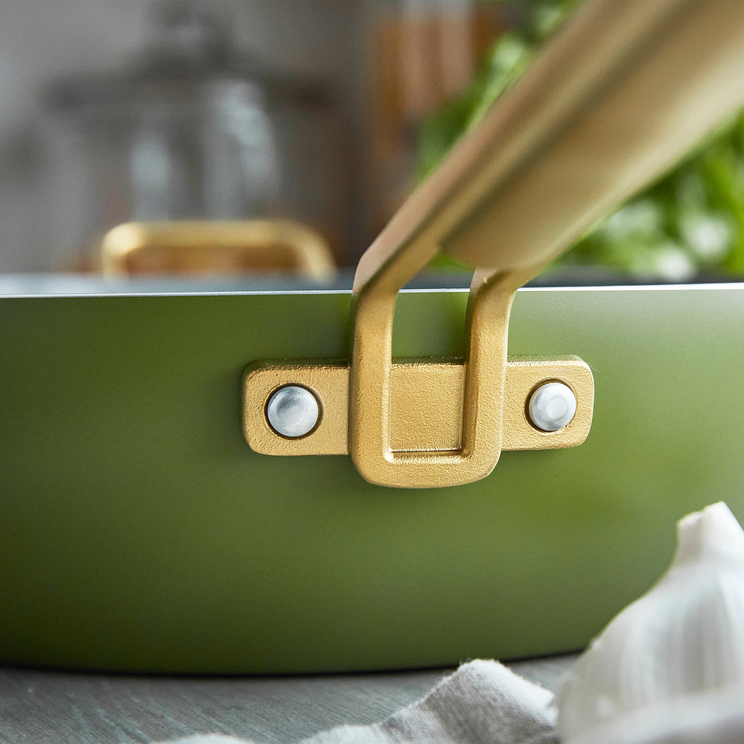 Close-up of a green pan with a gold handle on a blurred kitchen background.