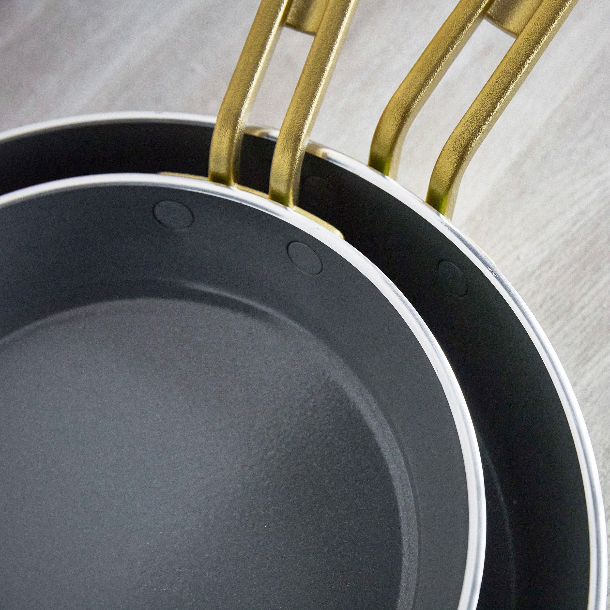 Two frying pans with gold handles on a light wooden surface