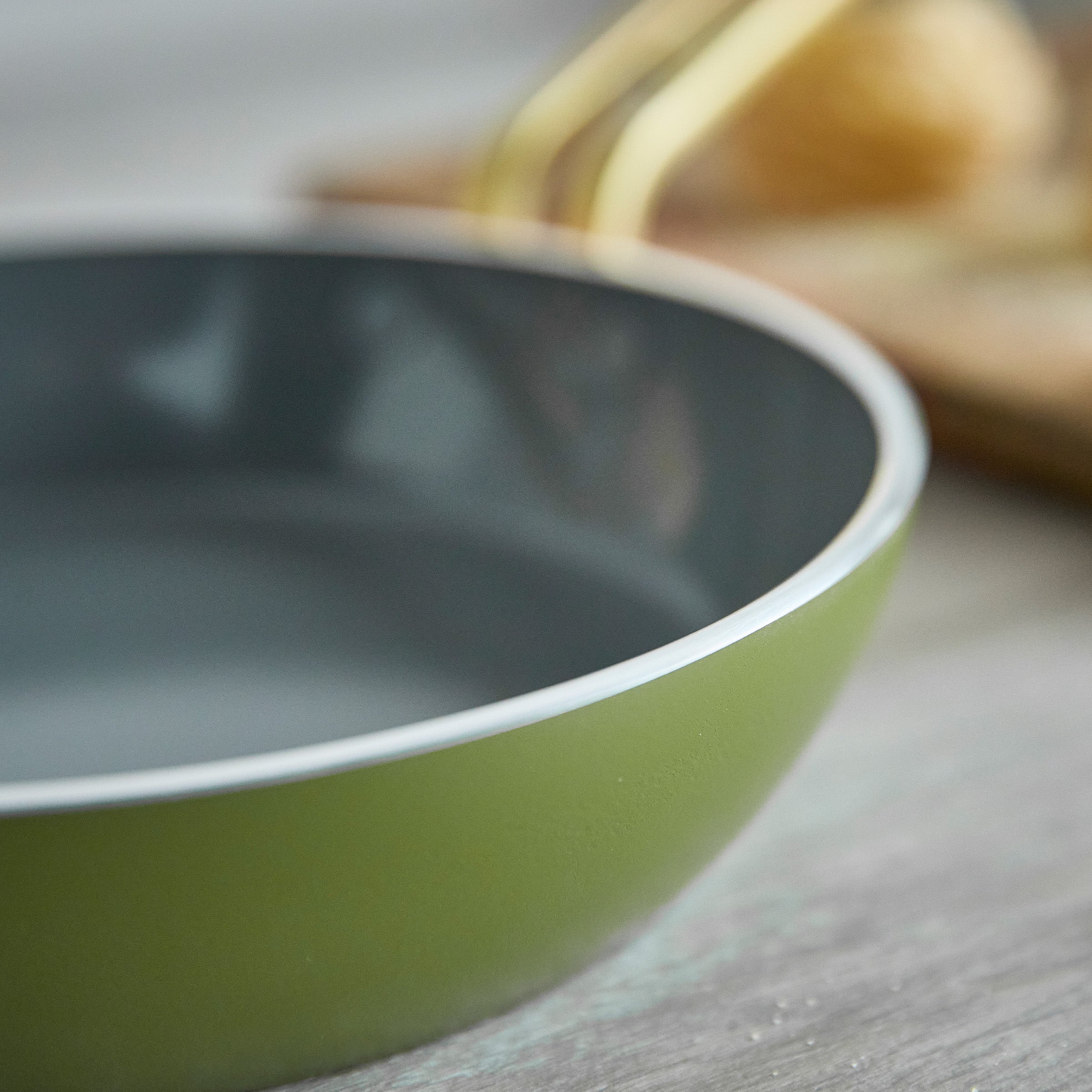 Green frying pan on a wooden surface with blurred background