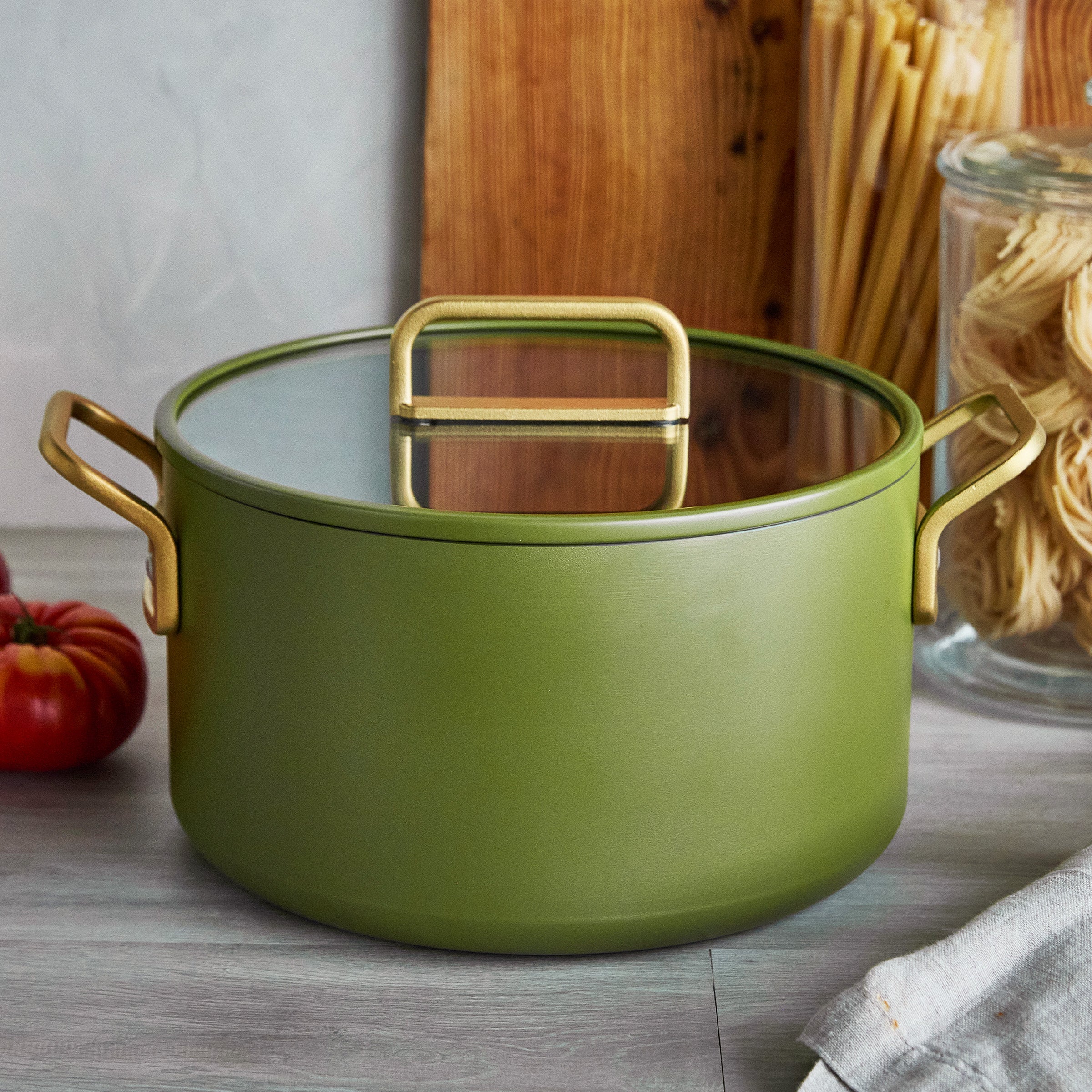 Green stockpot with gold handles on a wooden surface