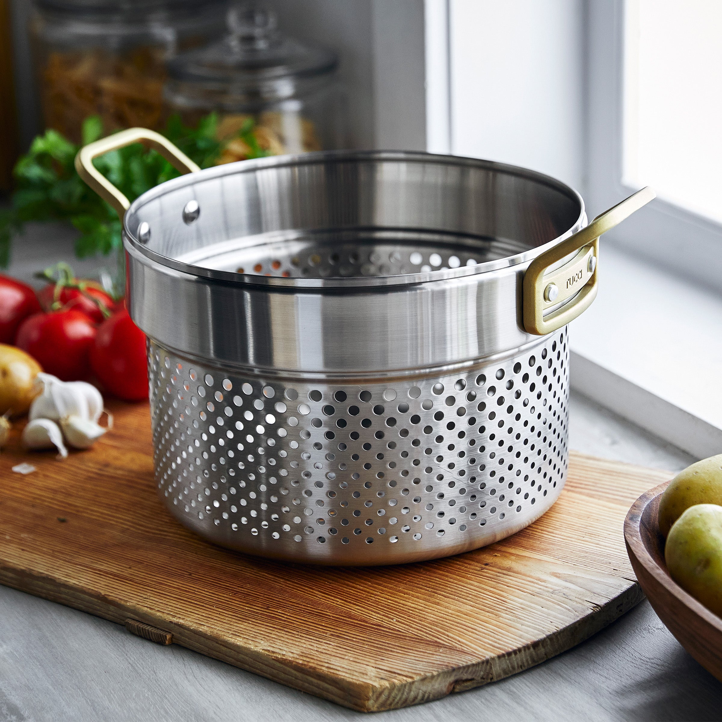 Stainless steel steamer on a wooden cutting board with vegetables in the background
