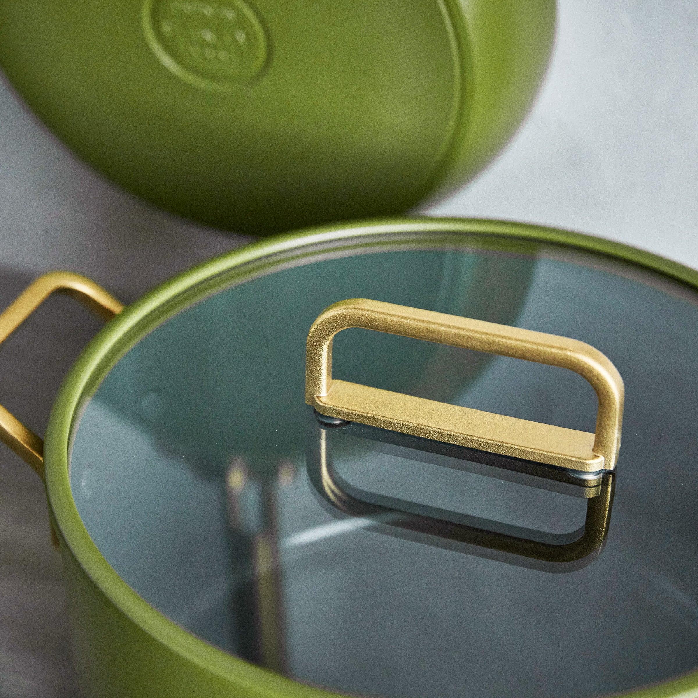Green stockpot with a glass lid and gold handles on a light gray background