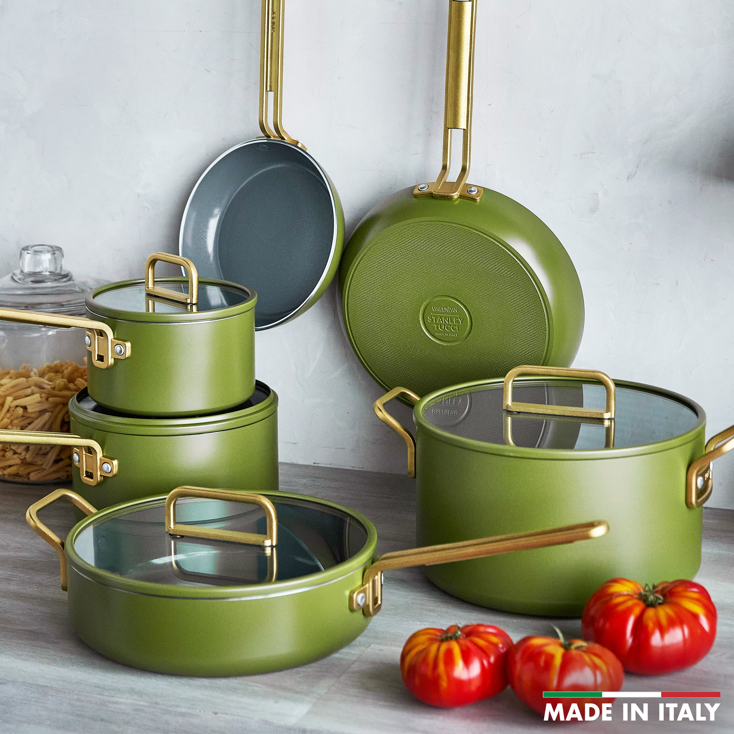 Set of green cookware with gold handles on a wooden surface with tomatoes.