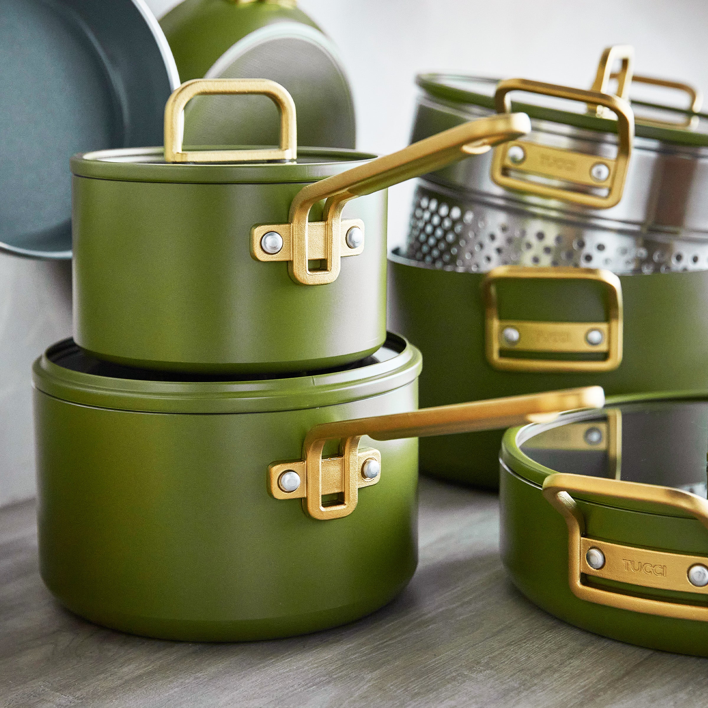Green cookware set with gold handles on a wooden surface