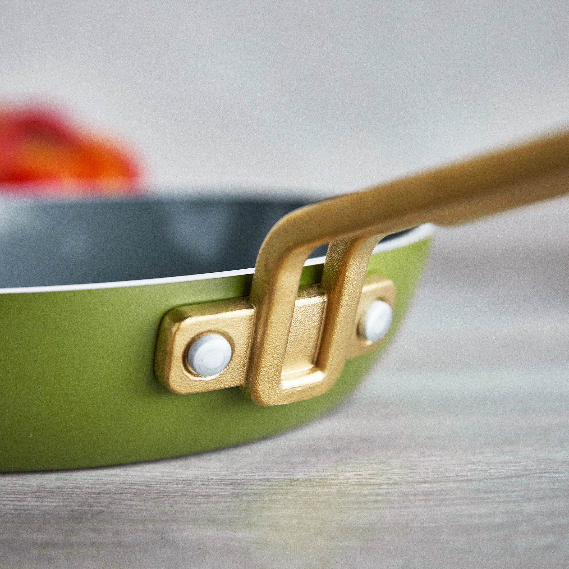 Close-up of a green frying pan with a gold handle on a wooden surface
