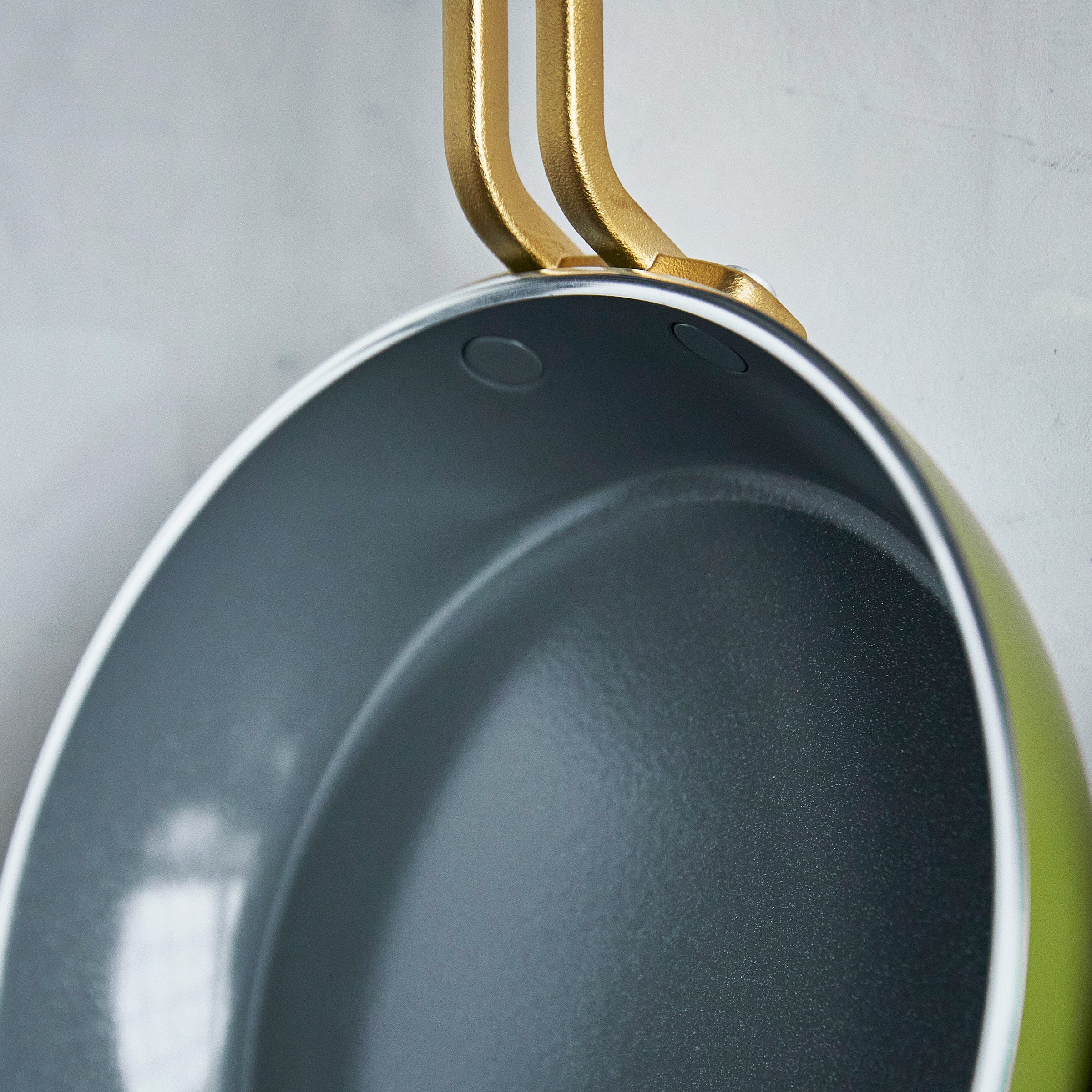Close-up of a green frying pan with gold handles on a light gray background