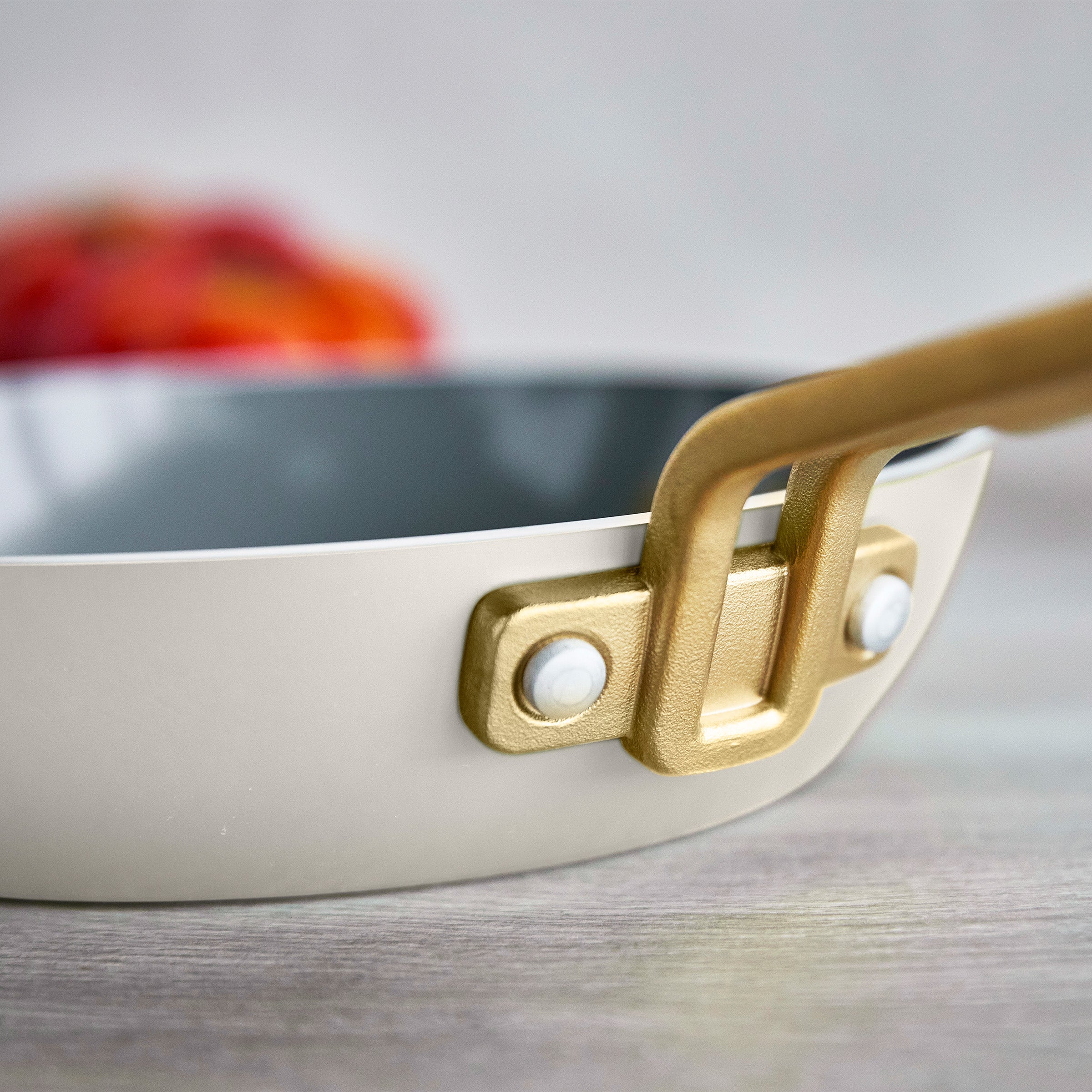 Close-up of a white frying pan with a gold handle on a neutral background