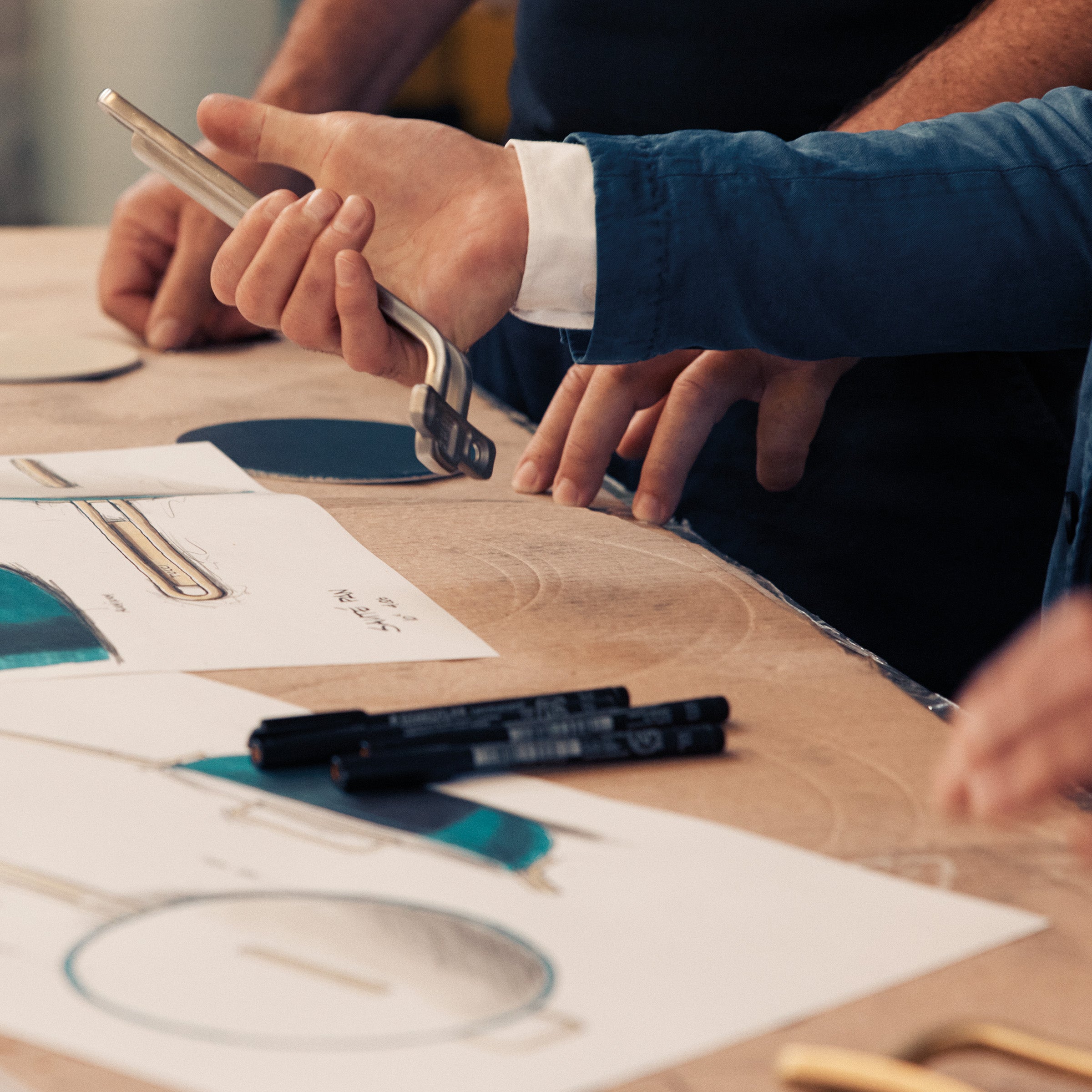 Two people working on a design project with blueprints and tools on a wooden table.