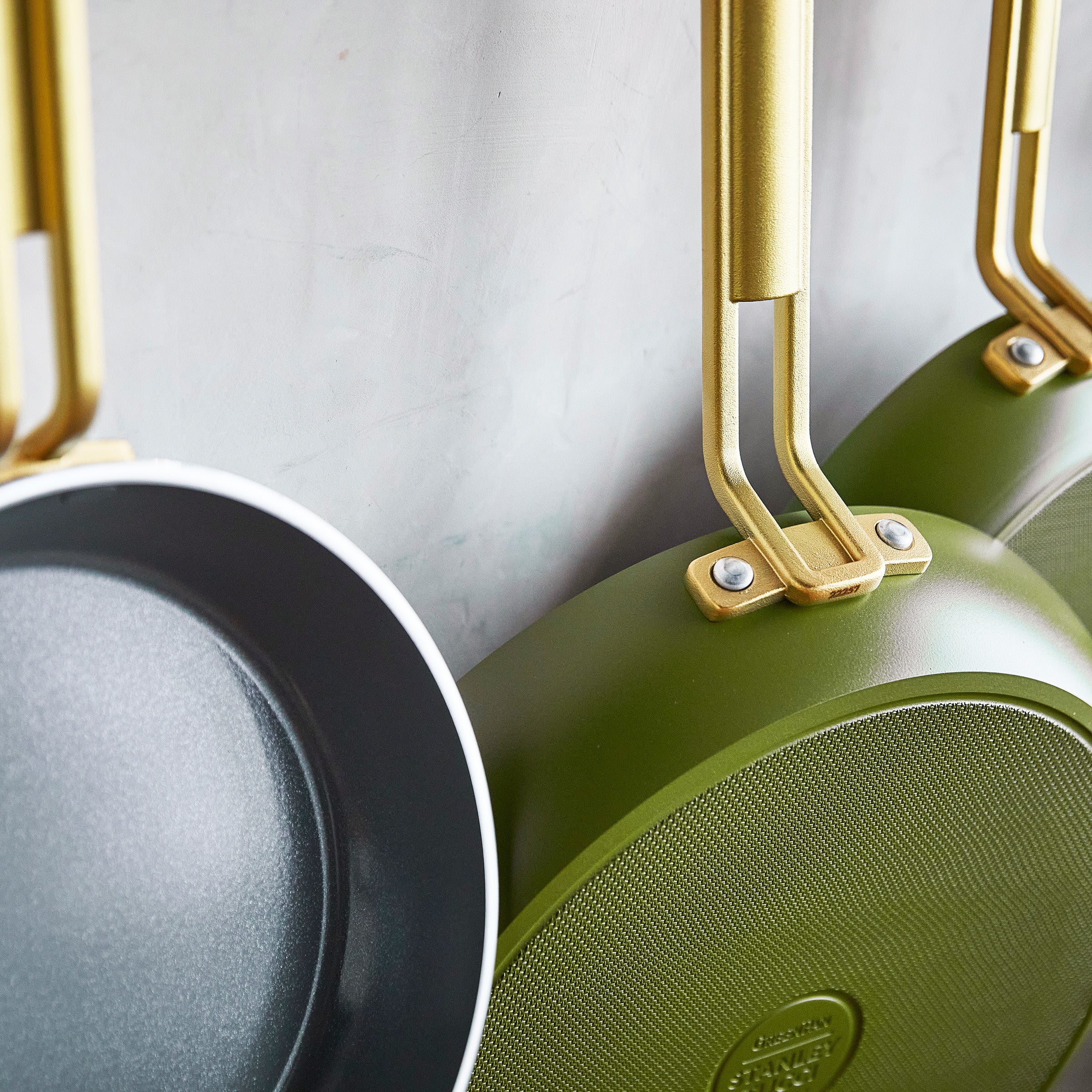 Green frying pans with gold handles on a light gray background