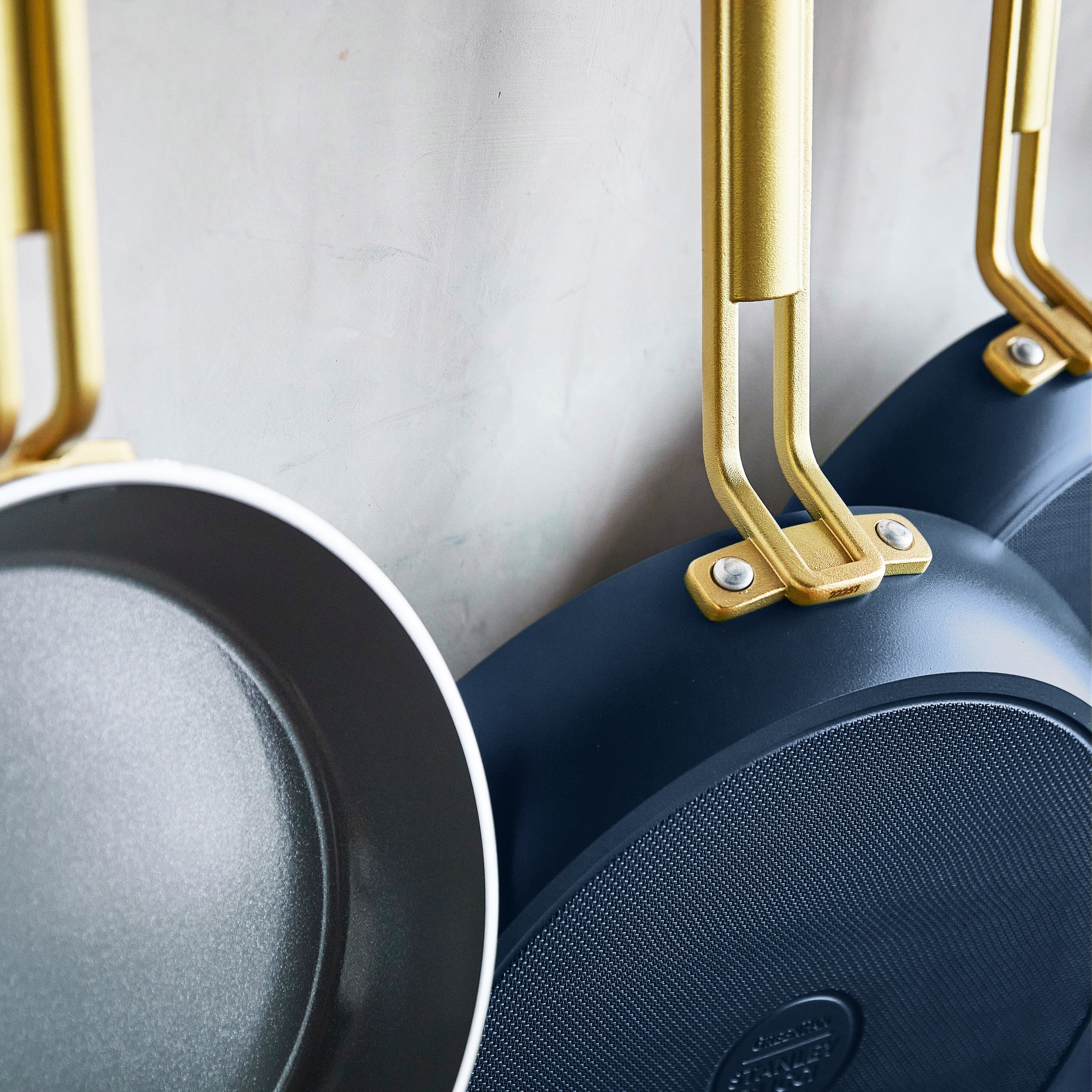 Set of blue frying pans with gold handles on a light gray background