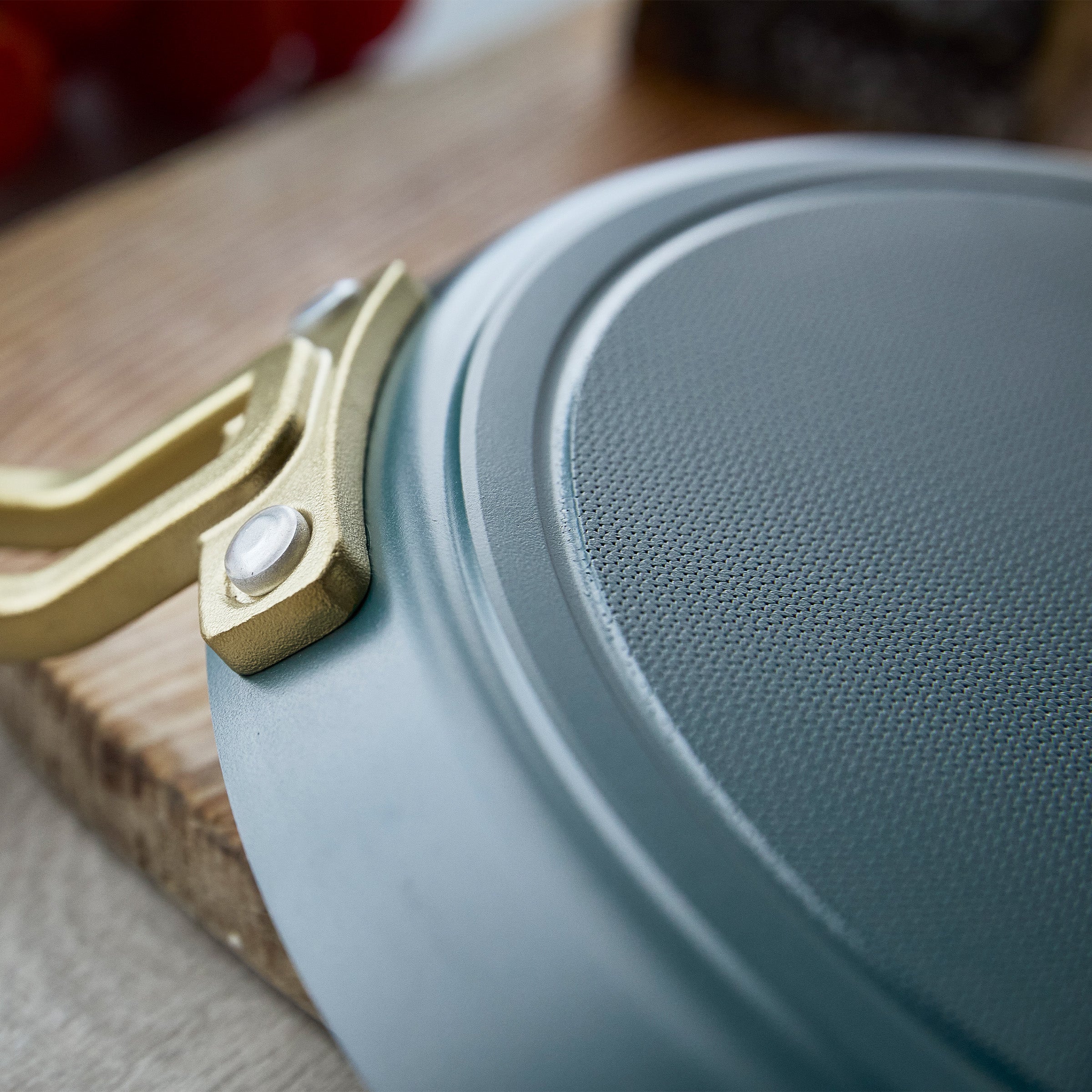 Close-up of a teal crepe pan with a gold handle on a wooden surface
