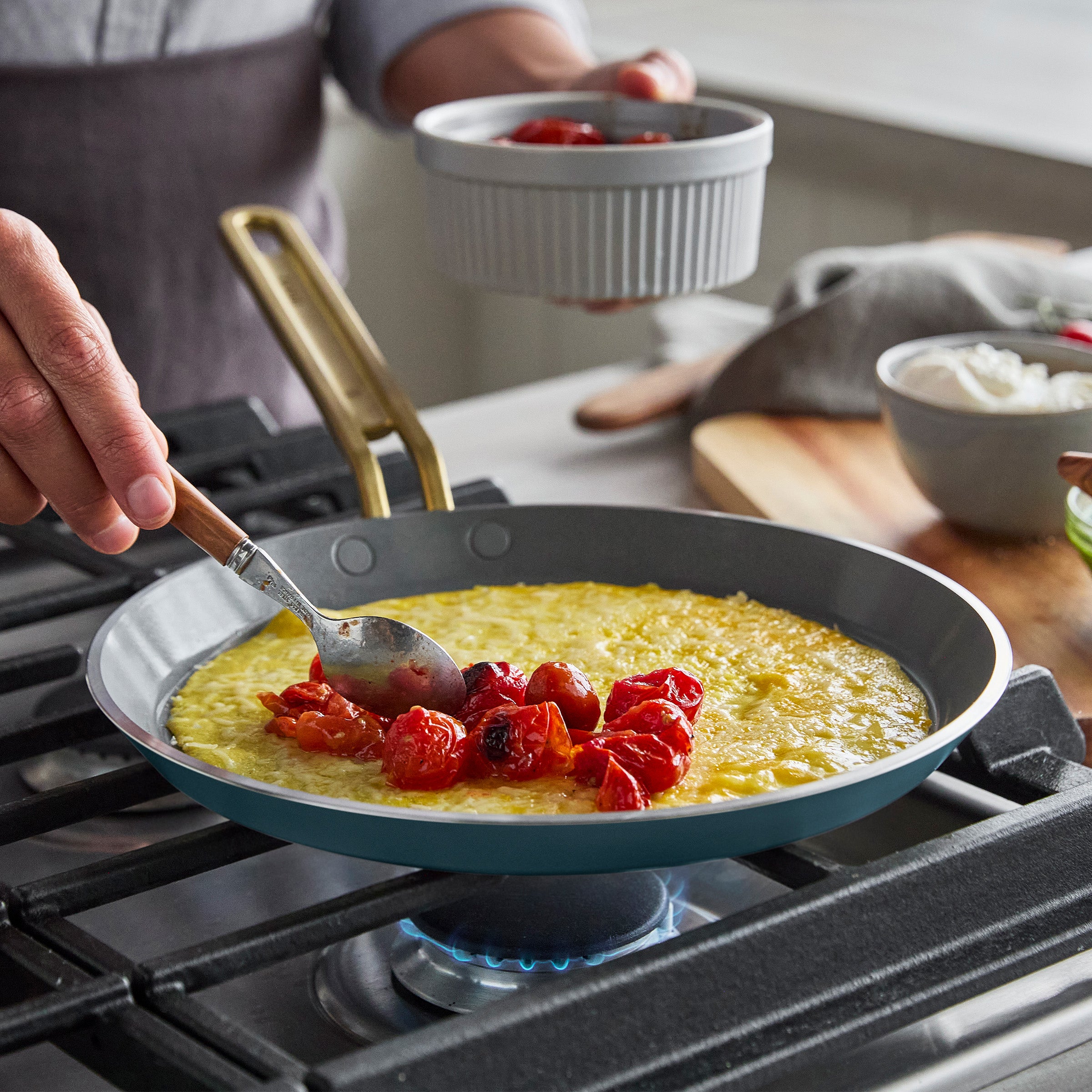 Person cooking a crepe with tomatoes in a pan on a stove
