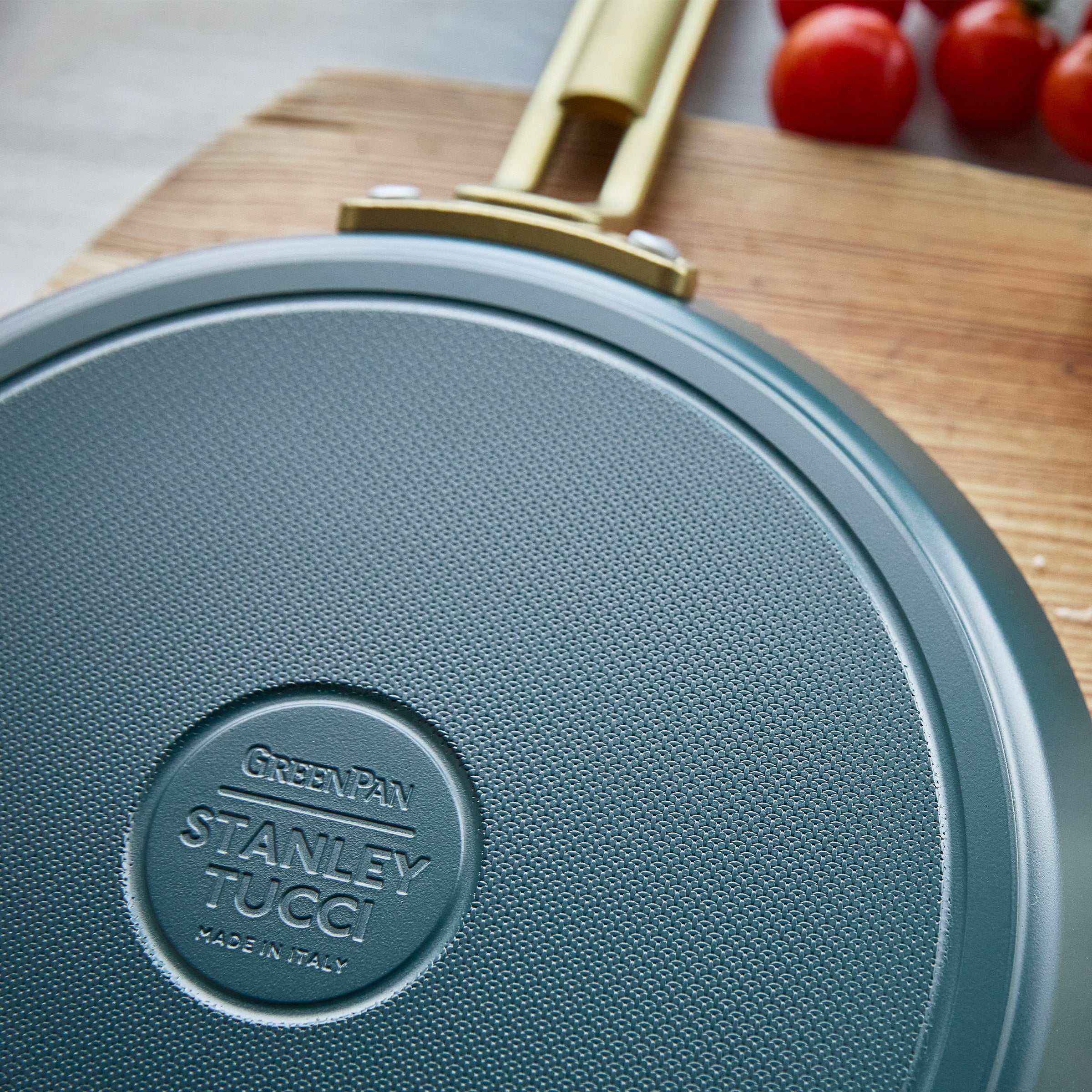 Teal crepe pan with a gold handle on a wooden cutting board with tomatoes