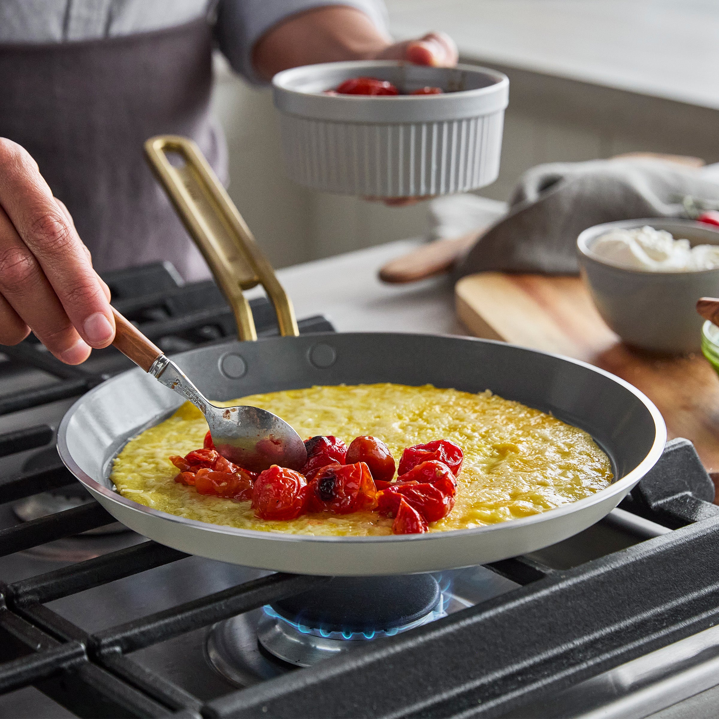 Person cooking eggs a crepe with tomatoes in a pan on a stove