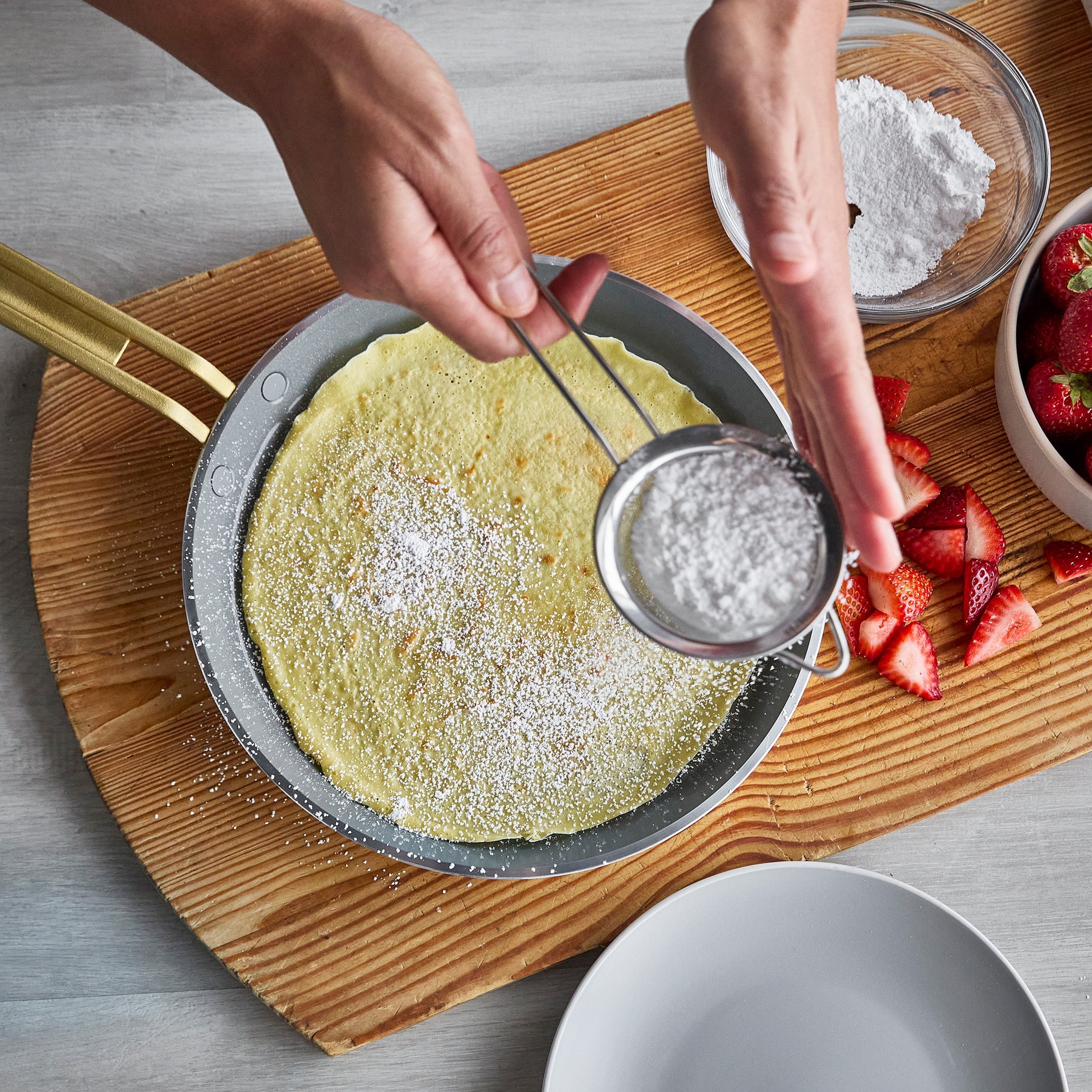 Person dusting a crepe with powdered sugar using a sifter