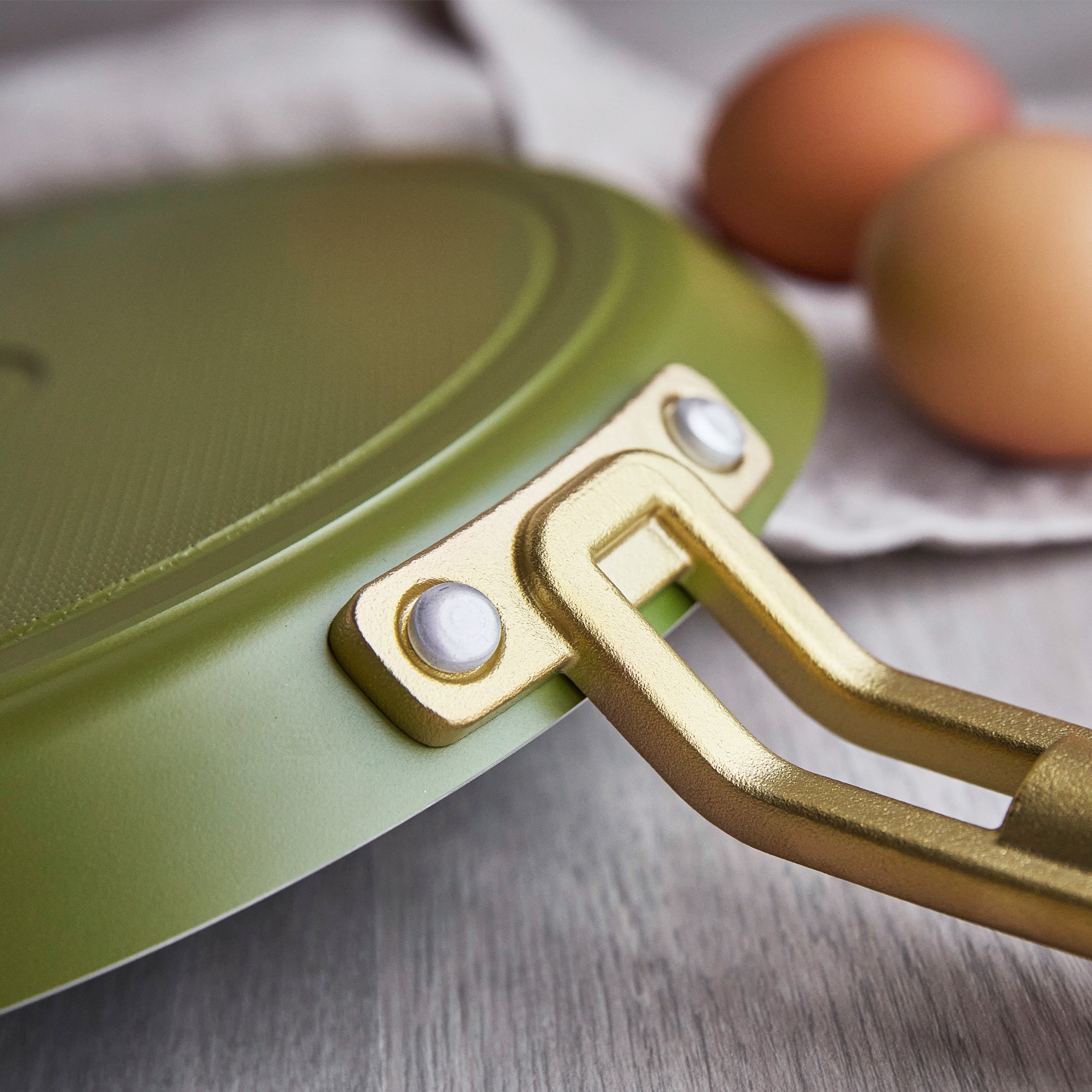 Close-up of a green crepe pan with a gold handle on a wooden surface.