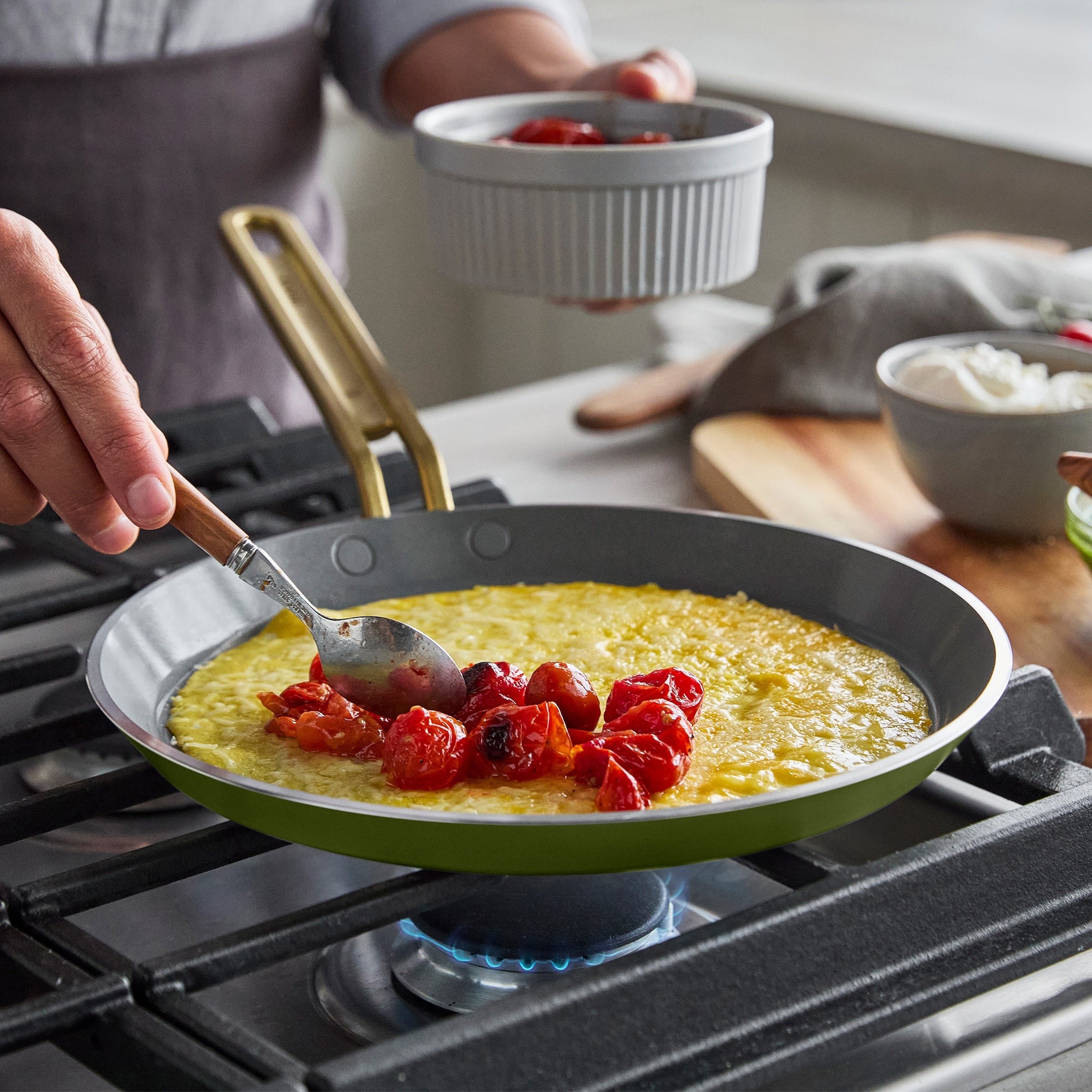 Person cooking a crepe with tomatoes in a pan on a stove