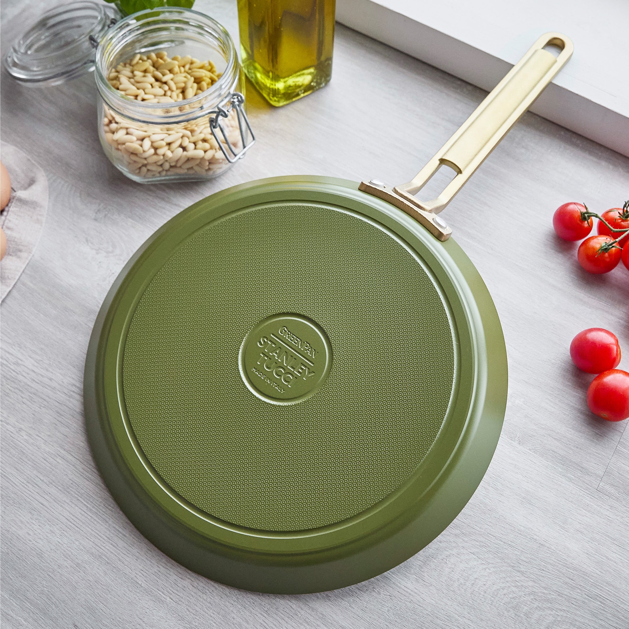 Green crepe pan with a gold handle on a light gray surface