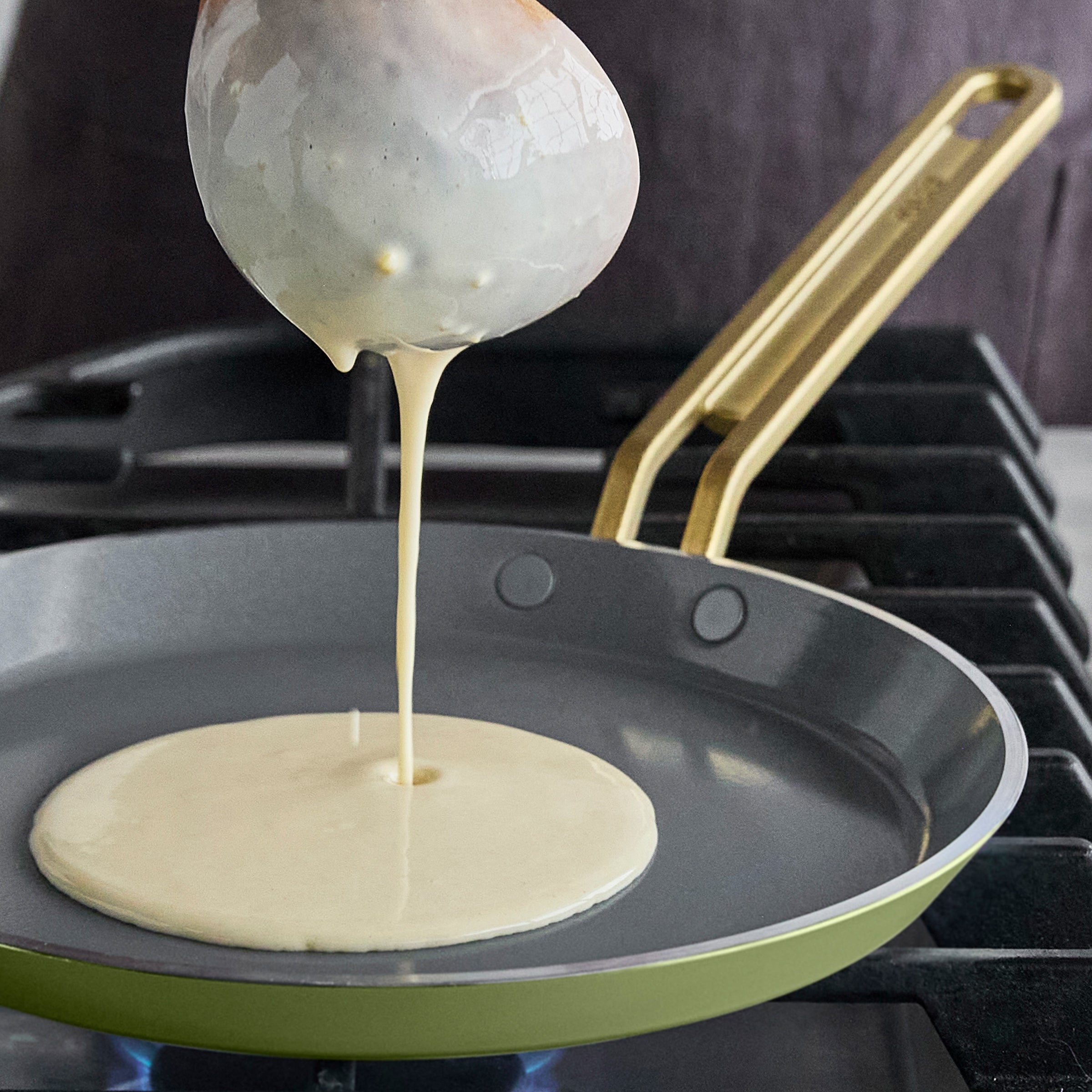 Crepe batter being poured from a ladle into a pan on a stovetop.