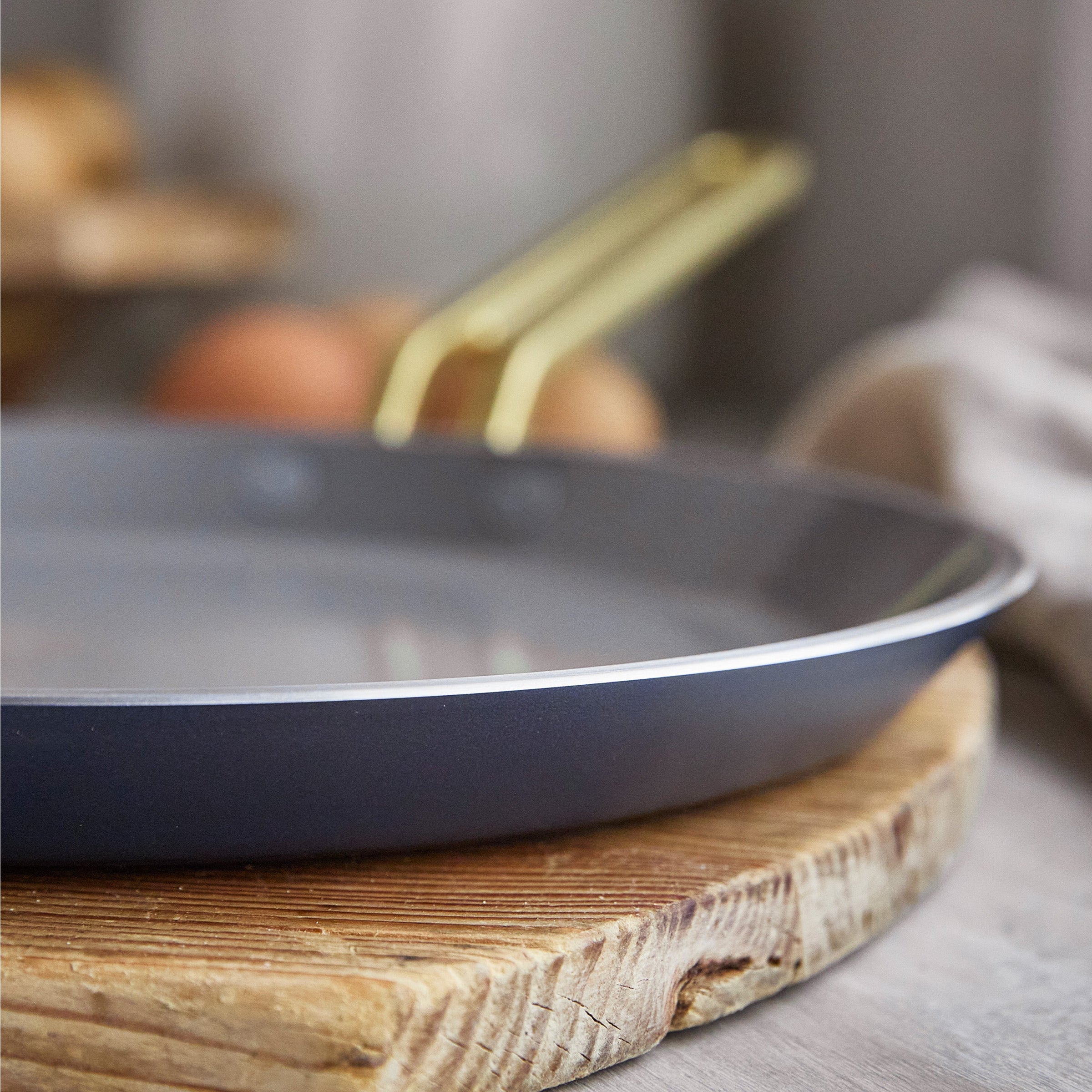 Blue crepe pan with a gold handle on a wooden surface