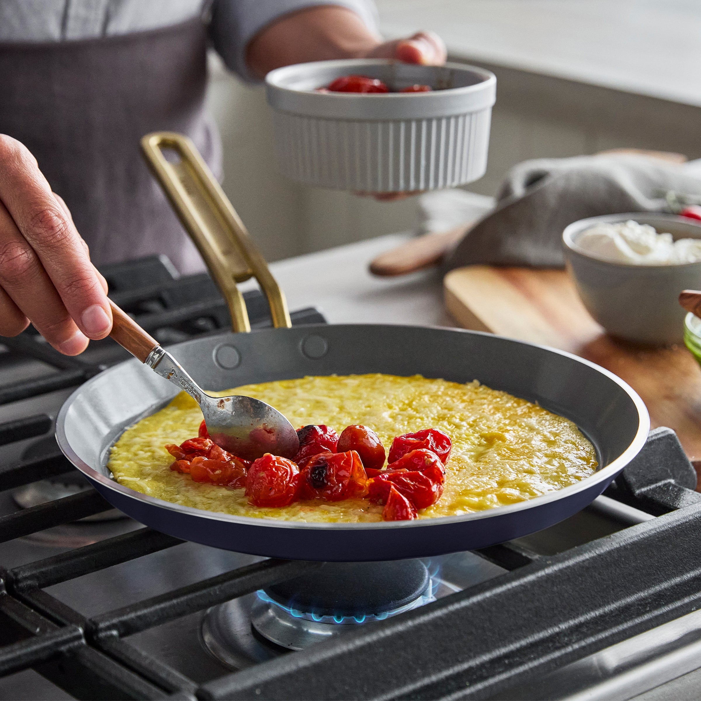 Person cooking a crepe with tomatoes in a pan on a stove