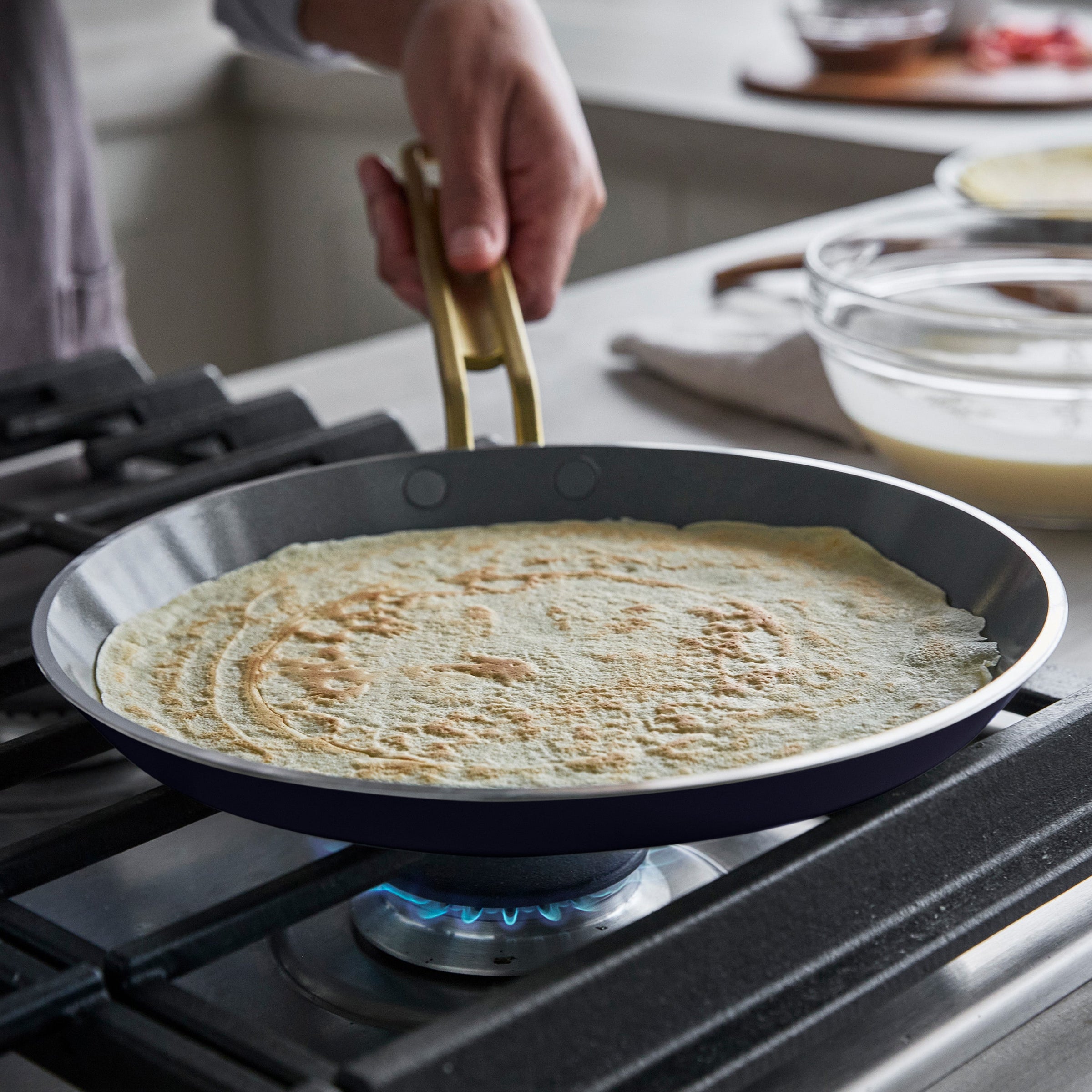 Person cooking a crepe on a pan over a gas stove