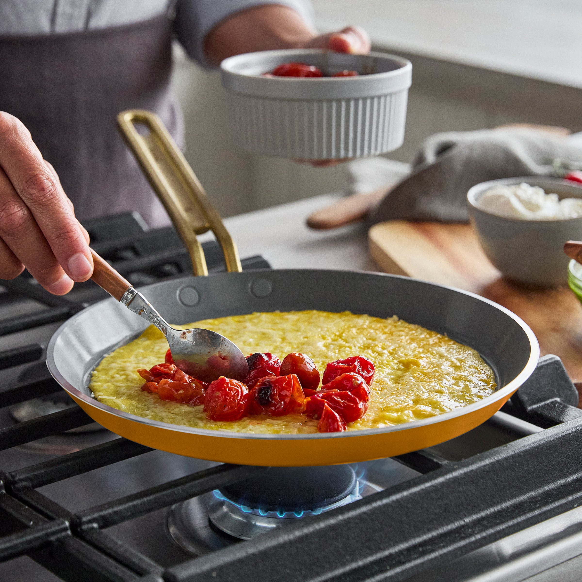 Person cooking a crepe with tomatoes in a pan on a stove