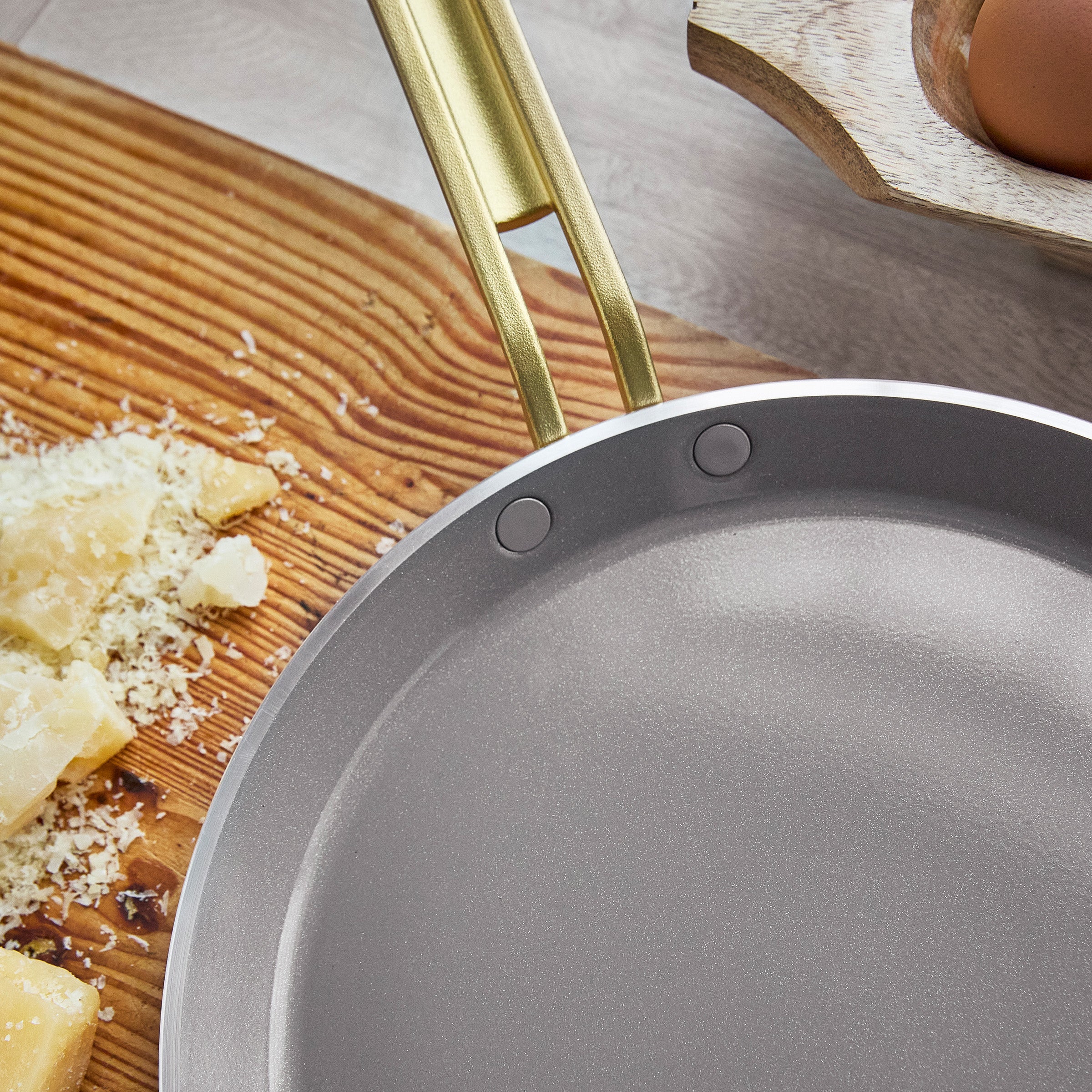 Crepe pan with gold handle on a wooden surface with cheese and eggs.